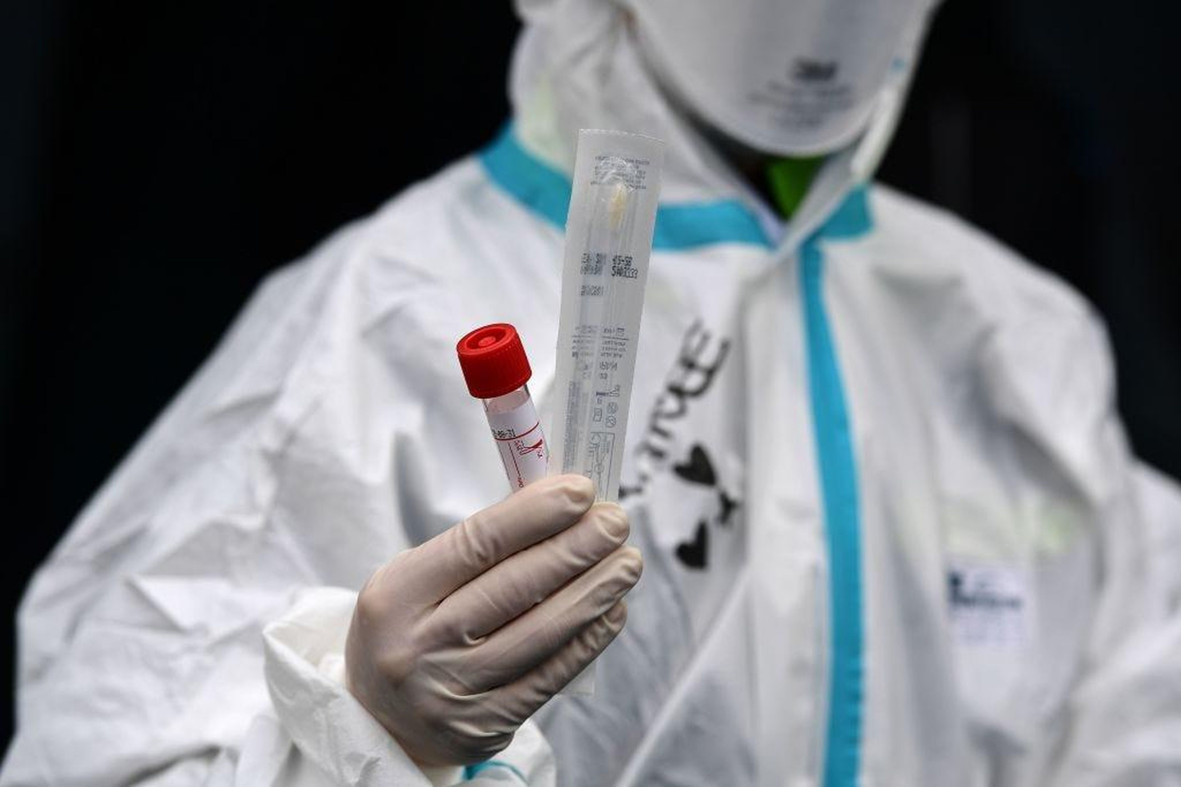 Un empleado del hospital con equipo de protección muestra un bastoncillo de algodón de una muestra de prueba de coronavirus.