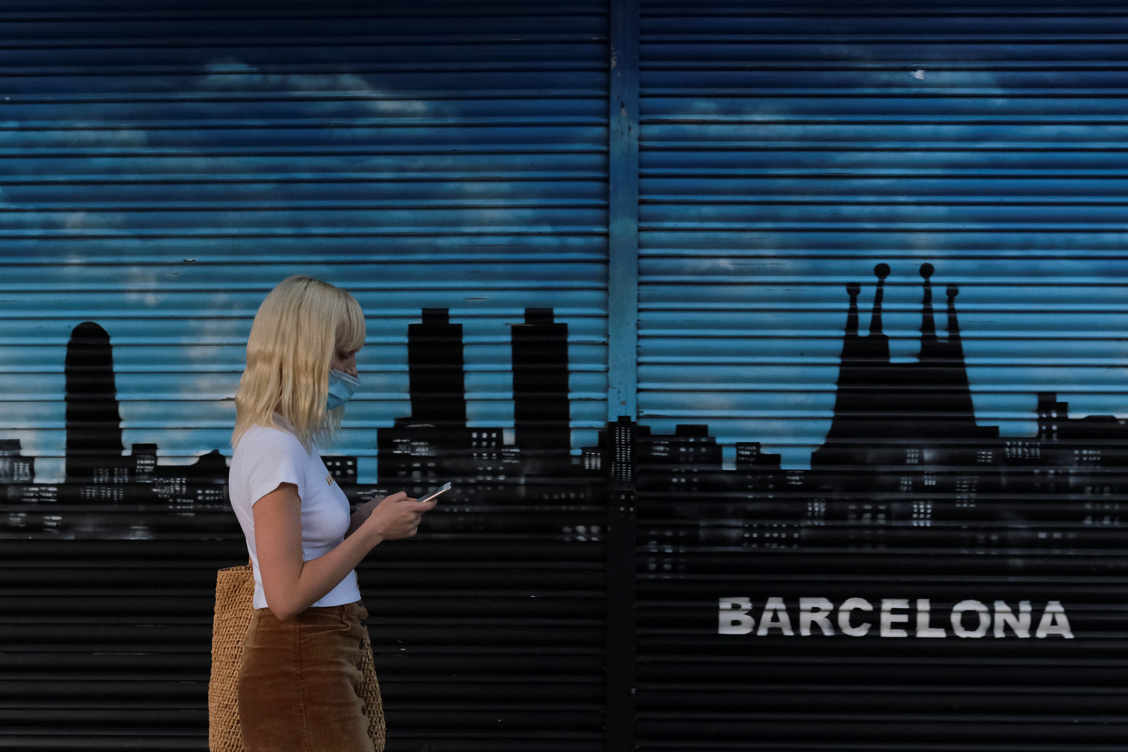 Una joven pasea con una mascarilla por delante de un mural pintado en Barcelona