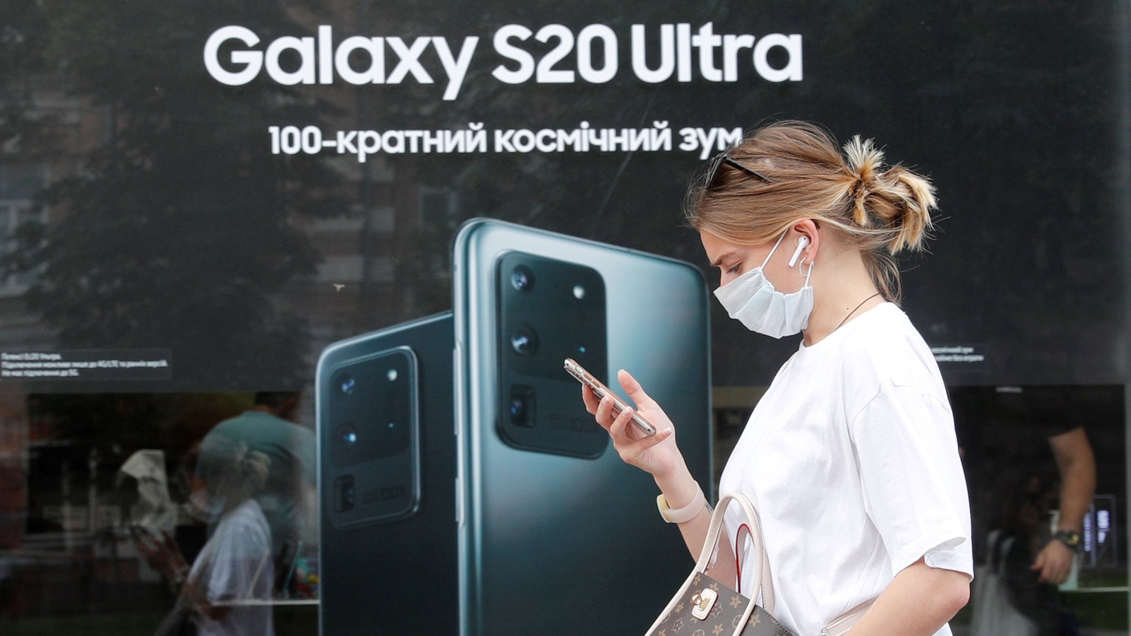 Una mujer con mascarilla camina delante de un cartel de Samsung.