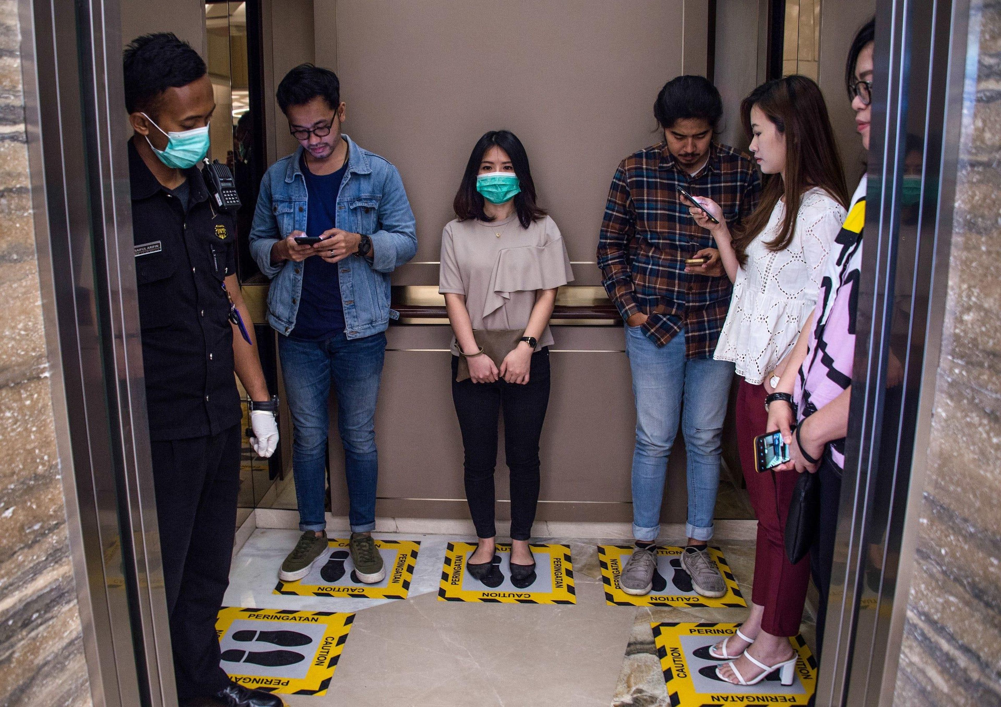 Personas en áreas designadas para asegurar el distanciamiento social dentro de un ascensor en un centro comercial en Surabaya, Indonesia, el 19 de marzo de 2020.