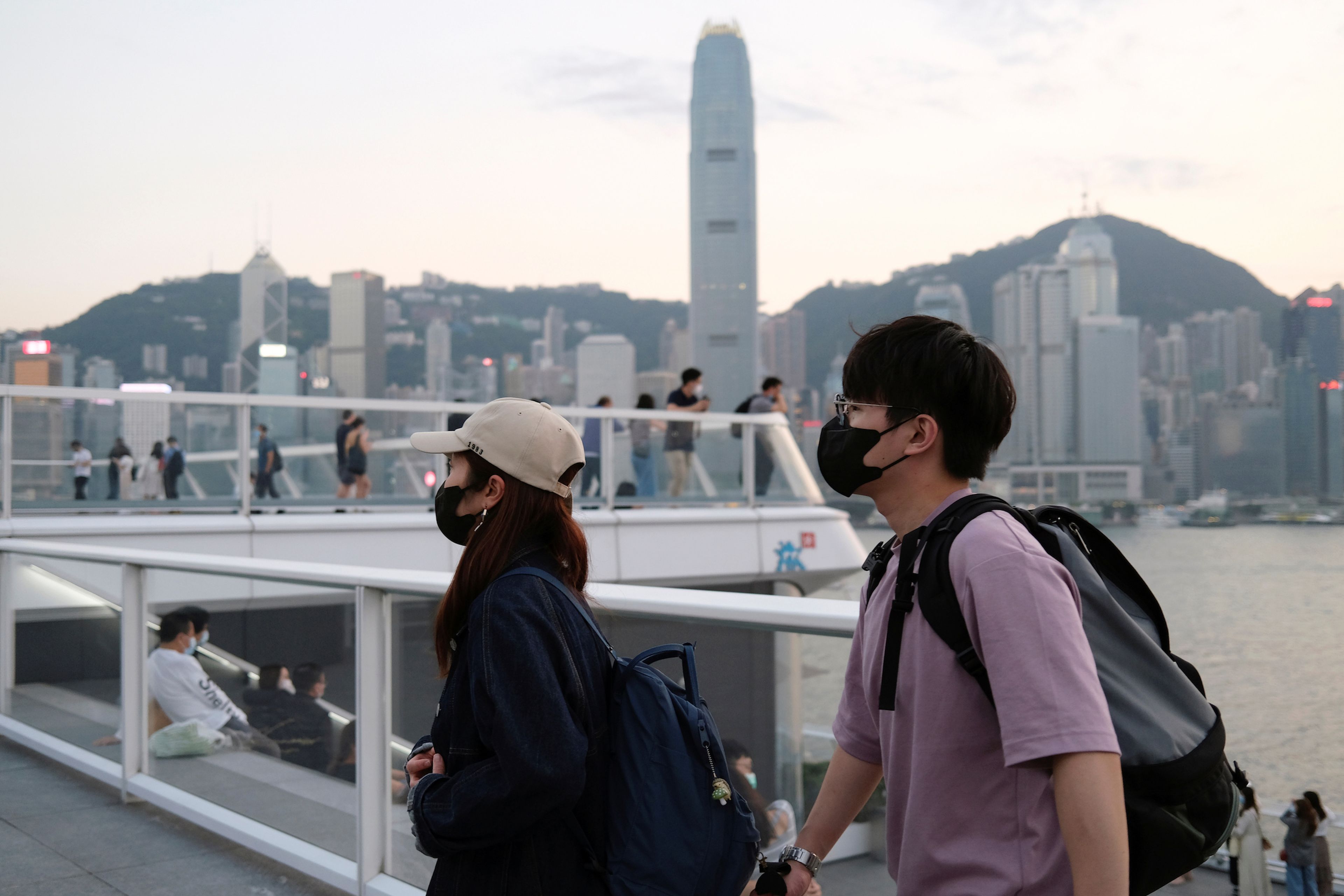 Personas con mascarillas caminan frente a los rascacielos de Hong Kong.