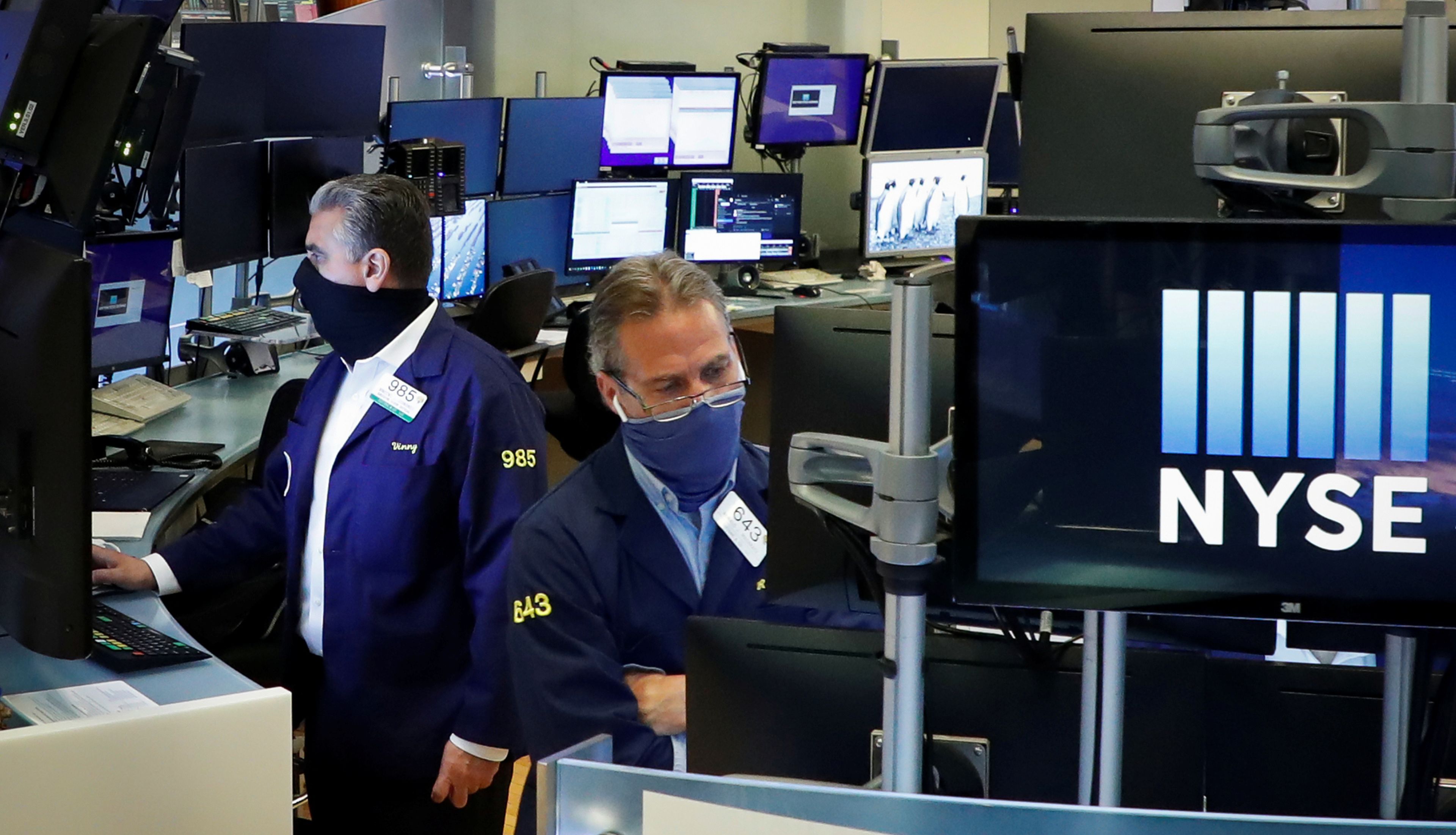Traders con mascarillas observan la cotización de las acciones en Wall Street