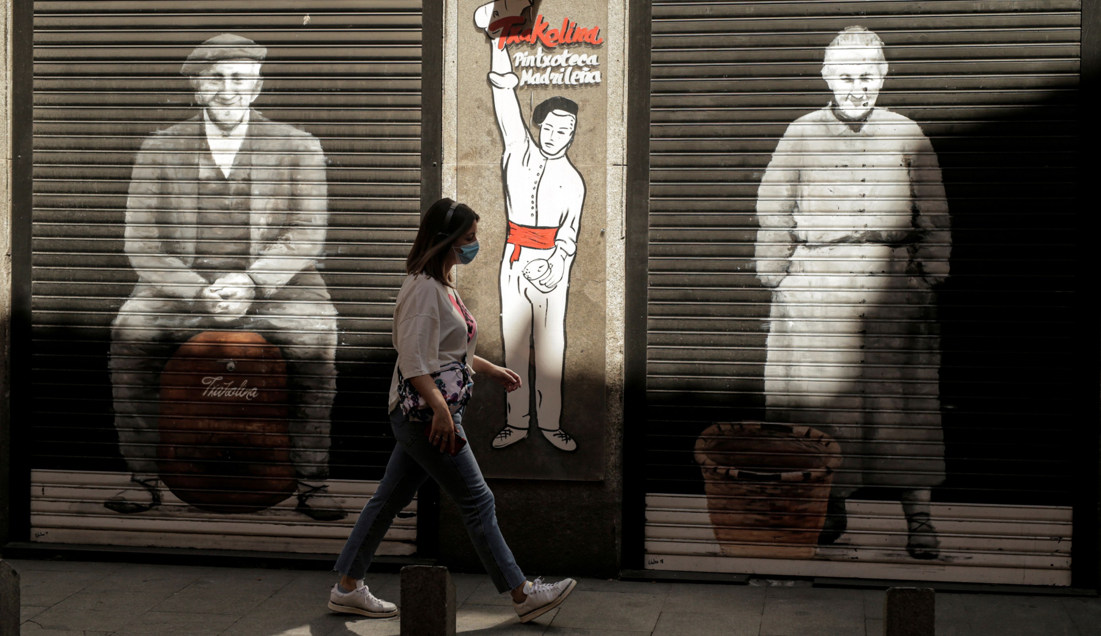 Una mujer con mascarilla pasa ante un bar cerrado en Madrid