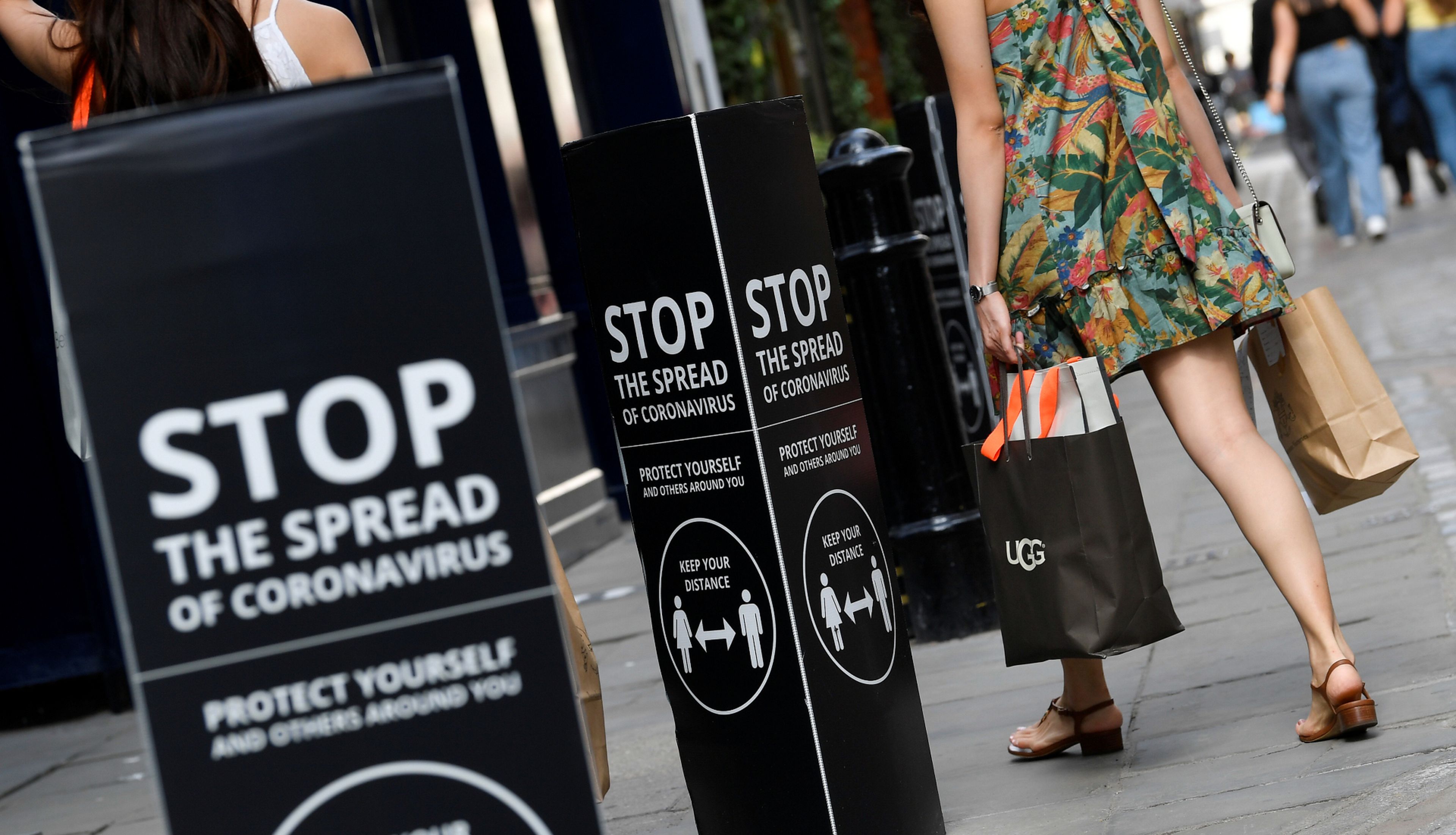 Una mujer pasa ante 2 anuncios sobre las precauciones contra el coronavirus en Londres