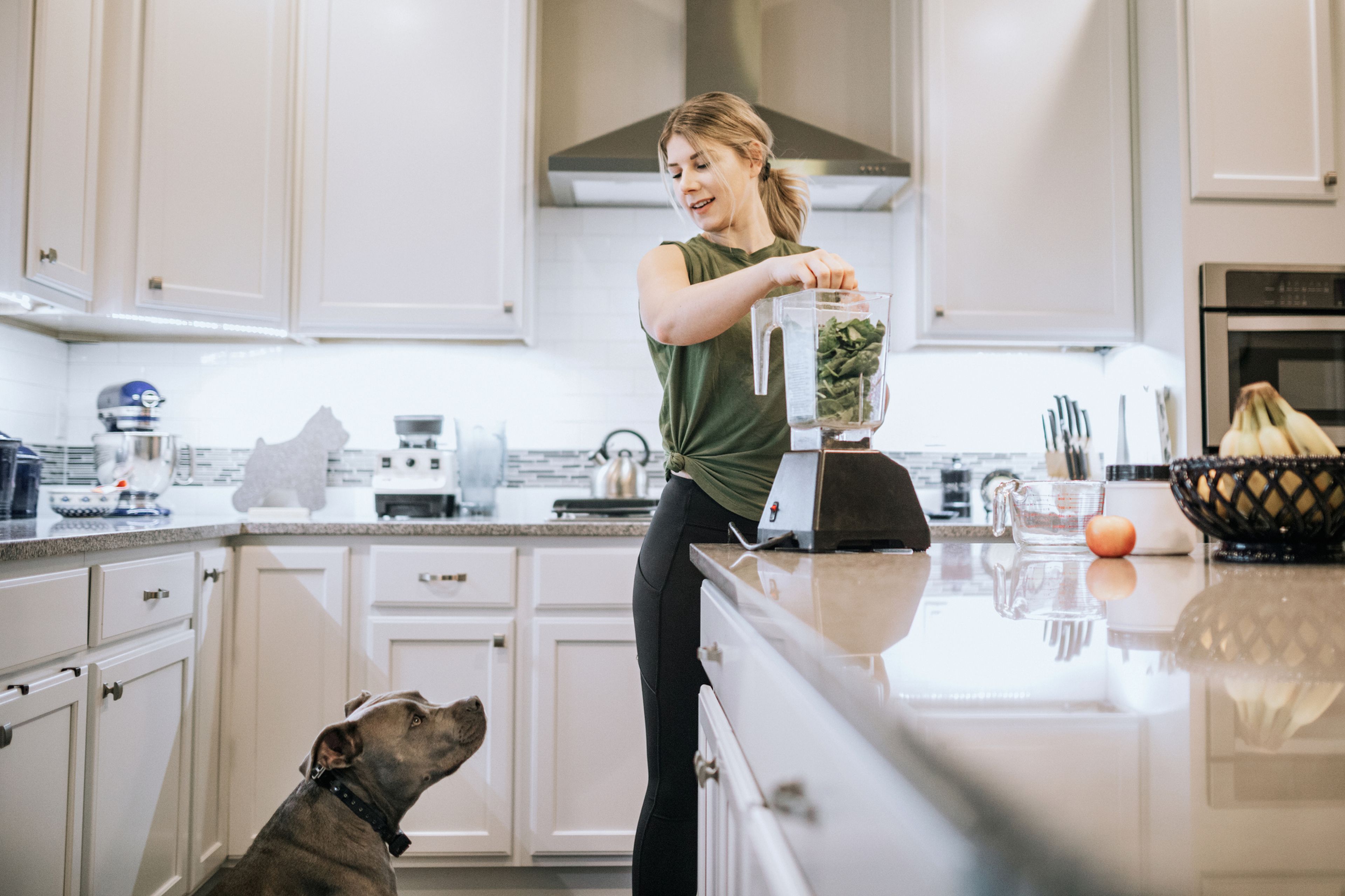 Una mujer con un perro en la cocina haciendo un batido de espinacas.