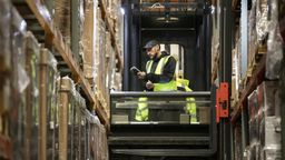 Un lavoratore mette i pacchi con un carrello elevatore a forche in un magazzino logistico