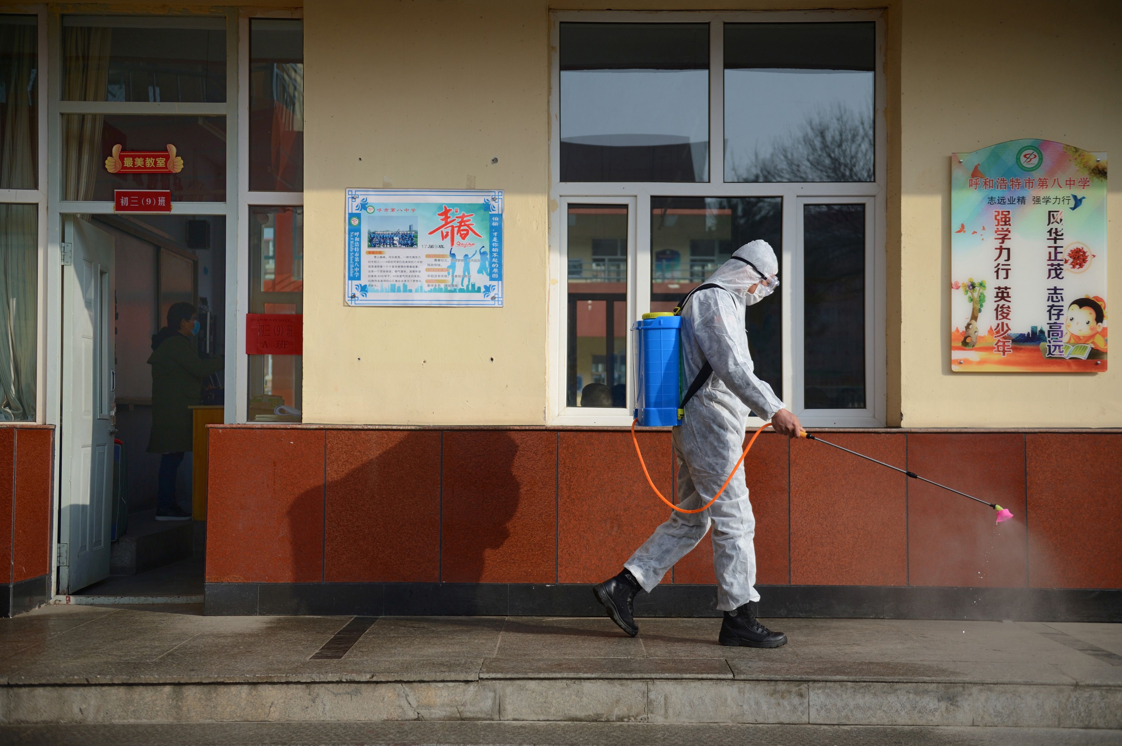 Un trabajador con traje protector rocía desinfectante en una escuela secundaria en Hohhot, China.