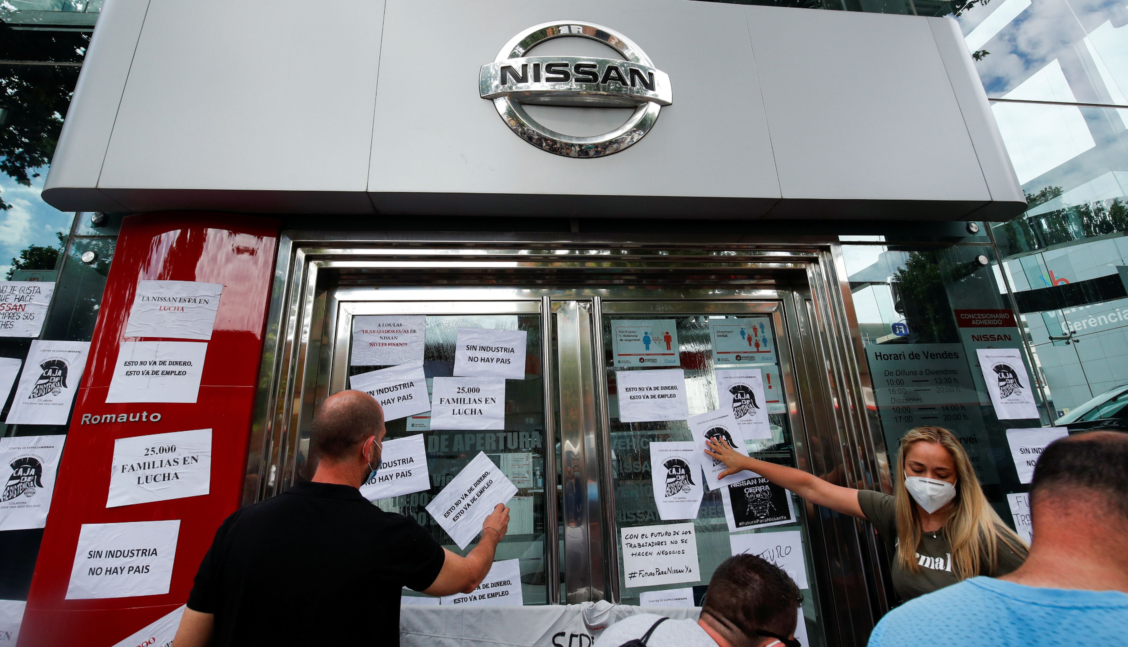 Trabajadores de Nissan pegan carteles contra el cierre de sus plantas en Barcelona en el escaparate de un concesionario de la marca nipona