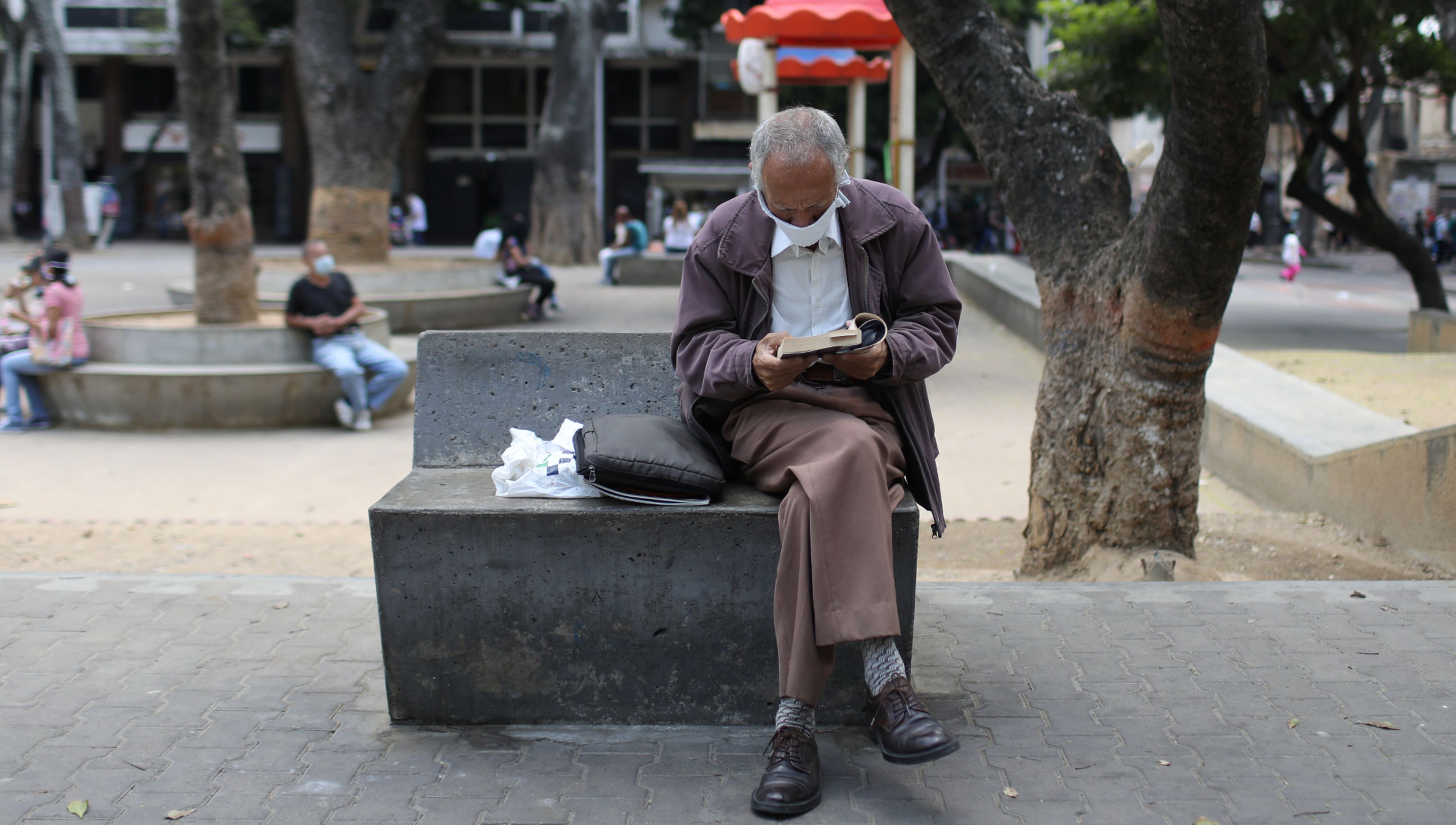 Un jubilado lee un libro en parque con una mascarilla puesta