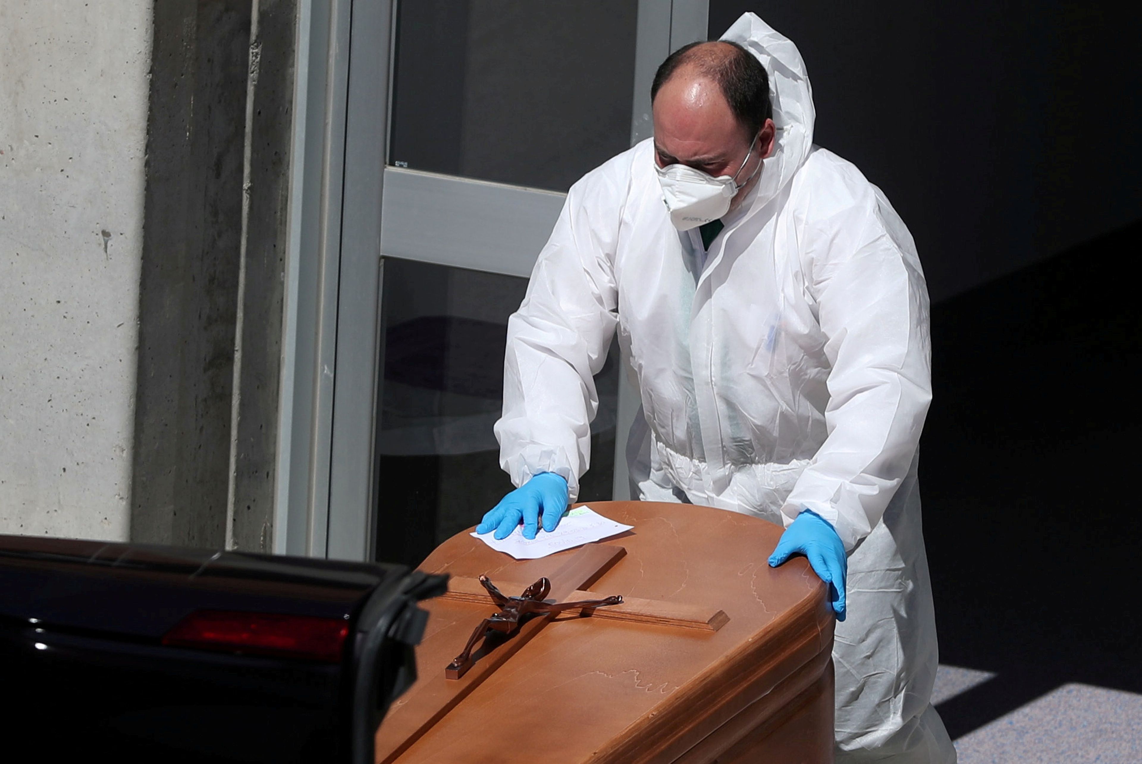Un trabajador funerario con traje protector saca un ataúd de la morgue del Hospital Severo Ochoa.