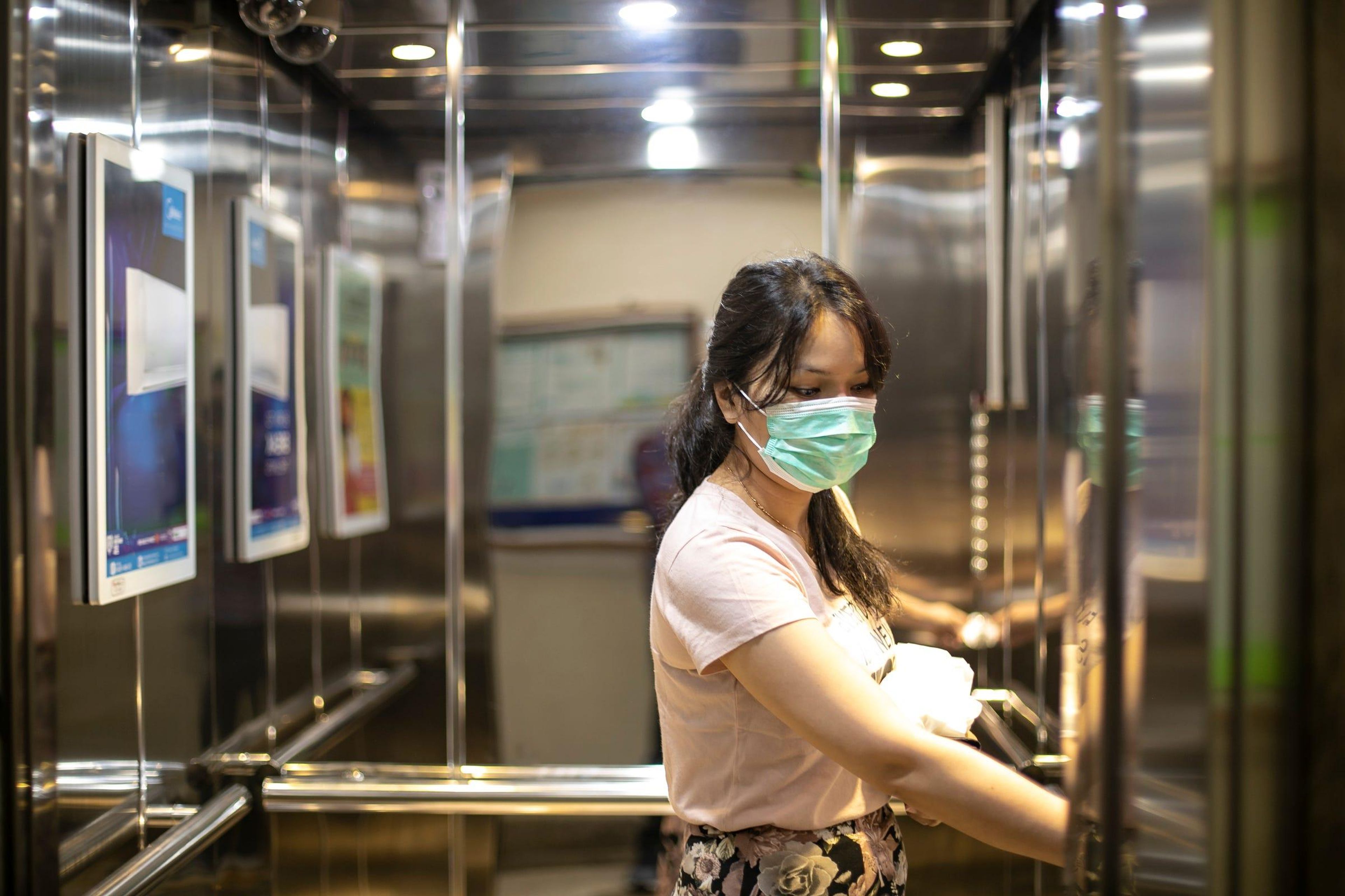 A young woman in an elevator wears a face mask to prevent coronavirus spread. Getty Images