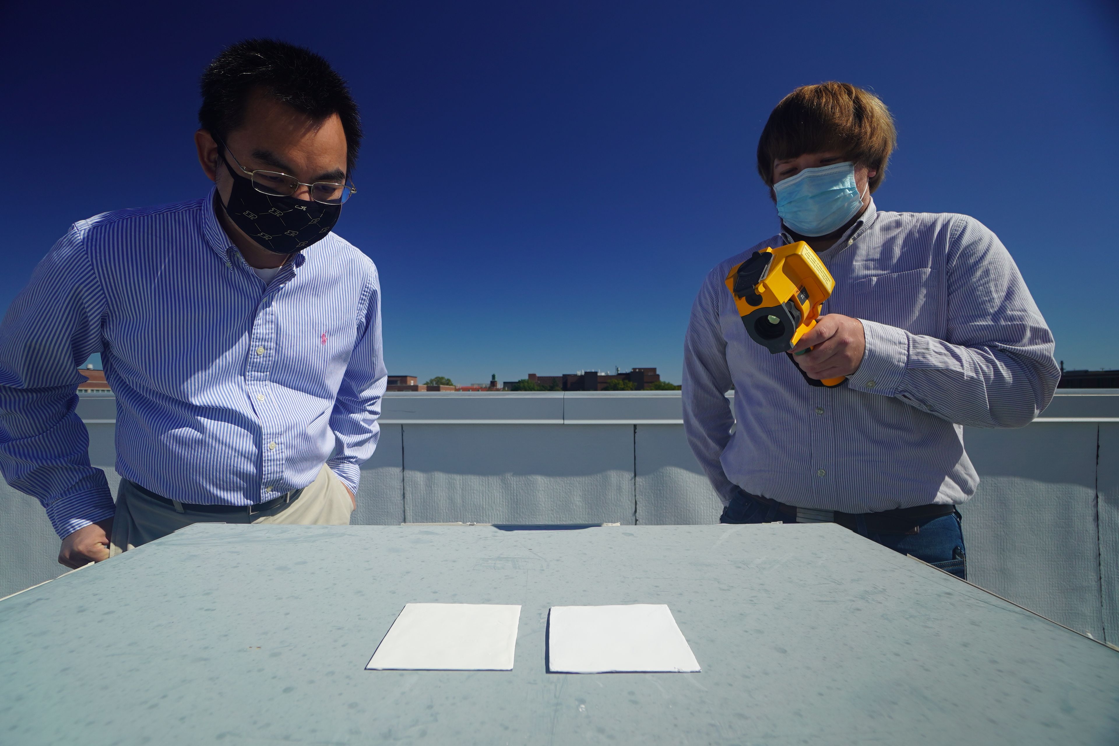 Xiulin Ruan (izquierda) y Joseph Peoples usan una cámara infrarroja para comparar el rendimiento de enfriamiento de las muestras de pintura blanca en un tejado.