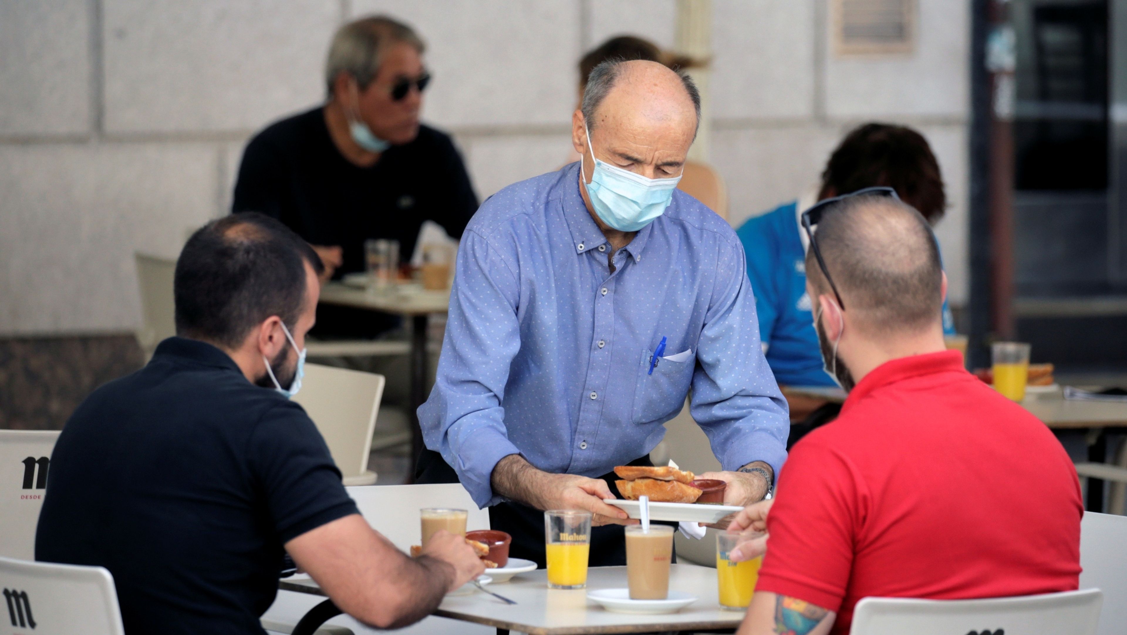 Un camarero sirve a 2 clientes con mascarilla en una terraza de Madrid