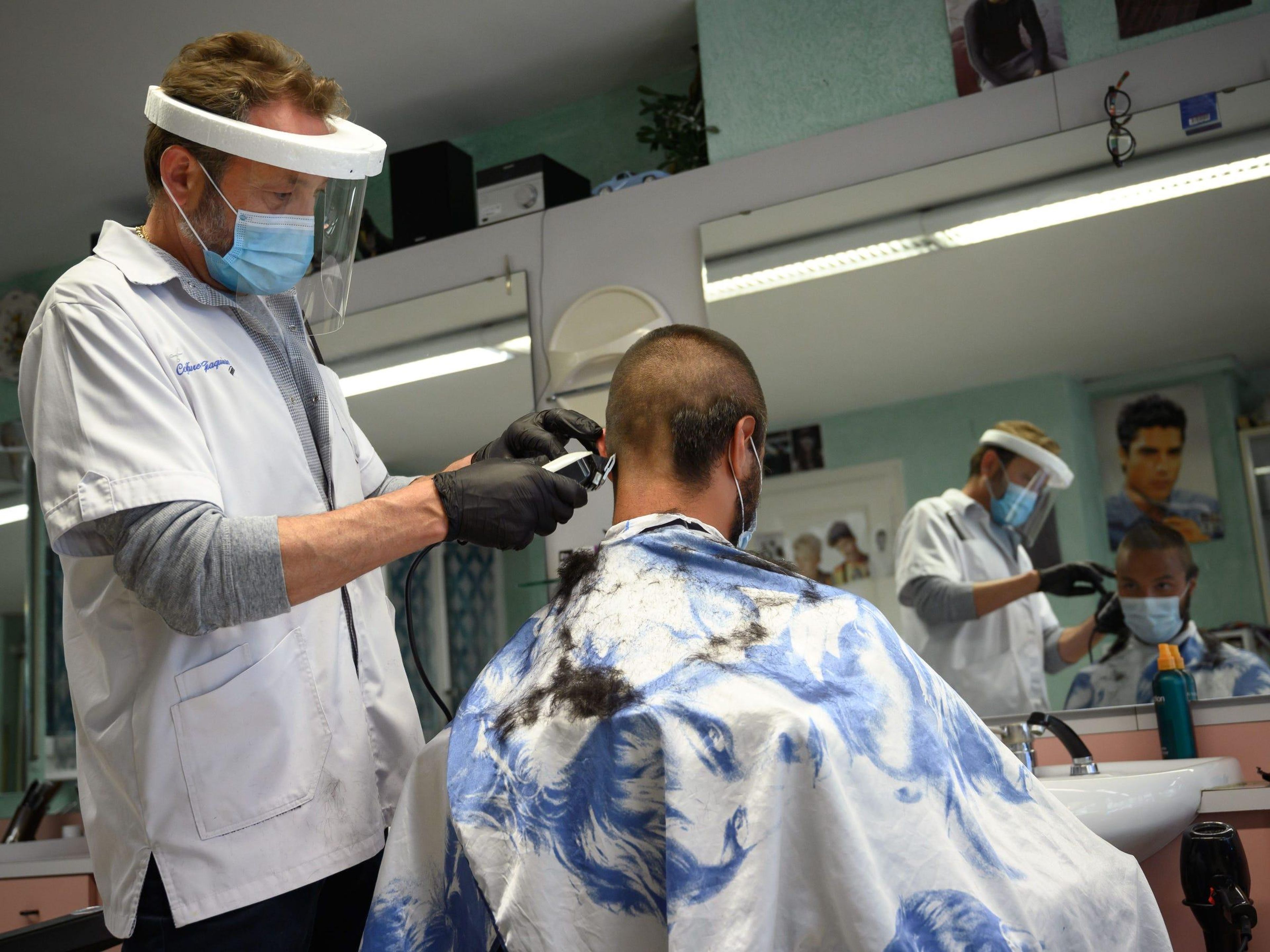 Un peluquero con mascarilla y pantalla protectora mientras corta el pelo.