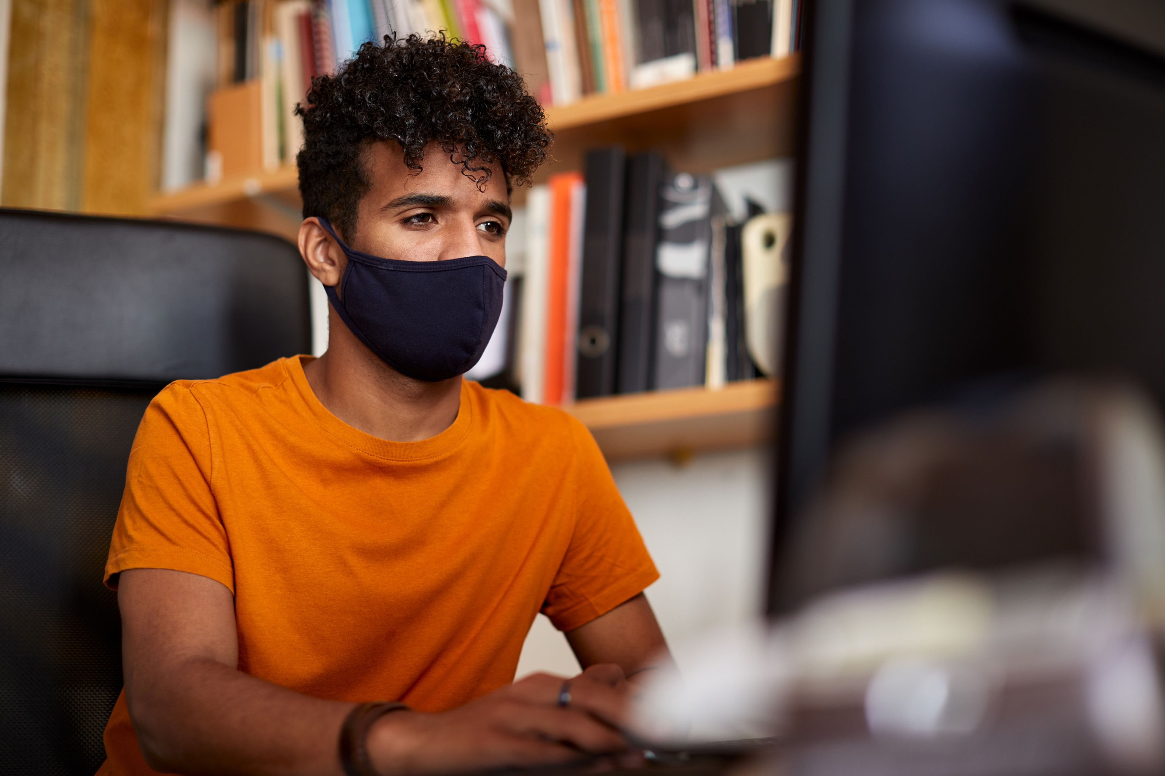 Un joven trabaja sentado frente a un ordenador con una mascarilla durante la pandemia del COVID-19