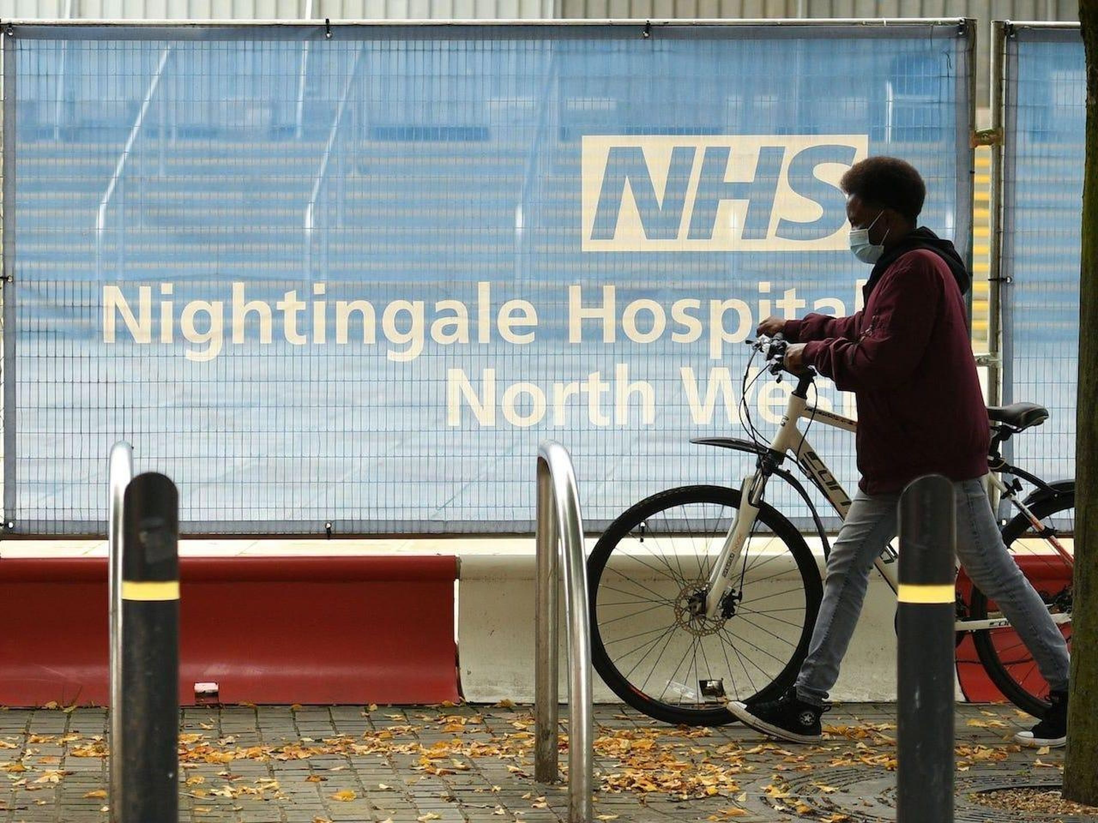 Un ciclista con mascarilla empuja una bicicleta a través de una barrera en las afueras del hospital de campo NHS Nightingale Hospital North West, establecido para proporcionar más capacidad hospitalaria durante la pandemia, el 13 de octubre de 2020.