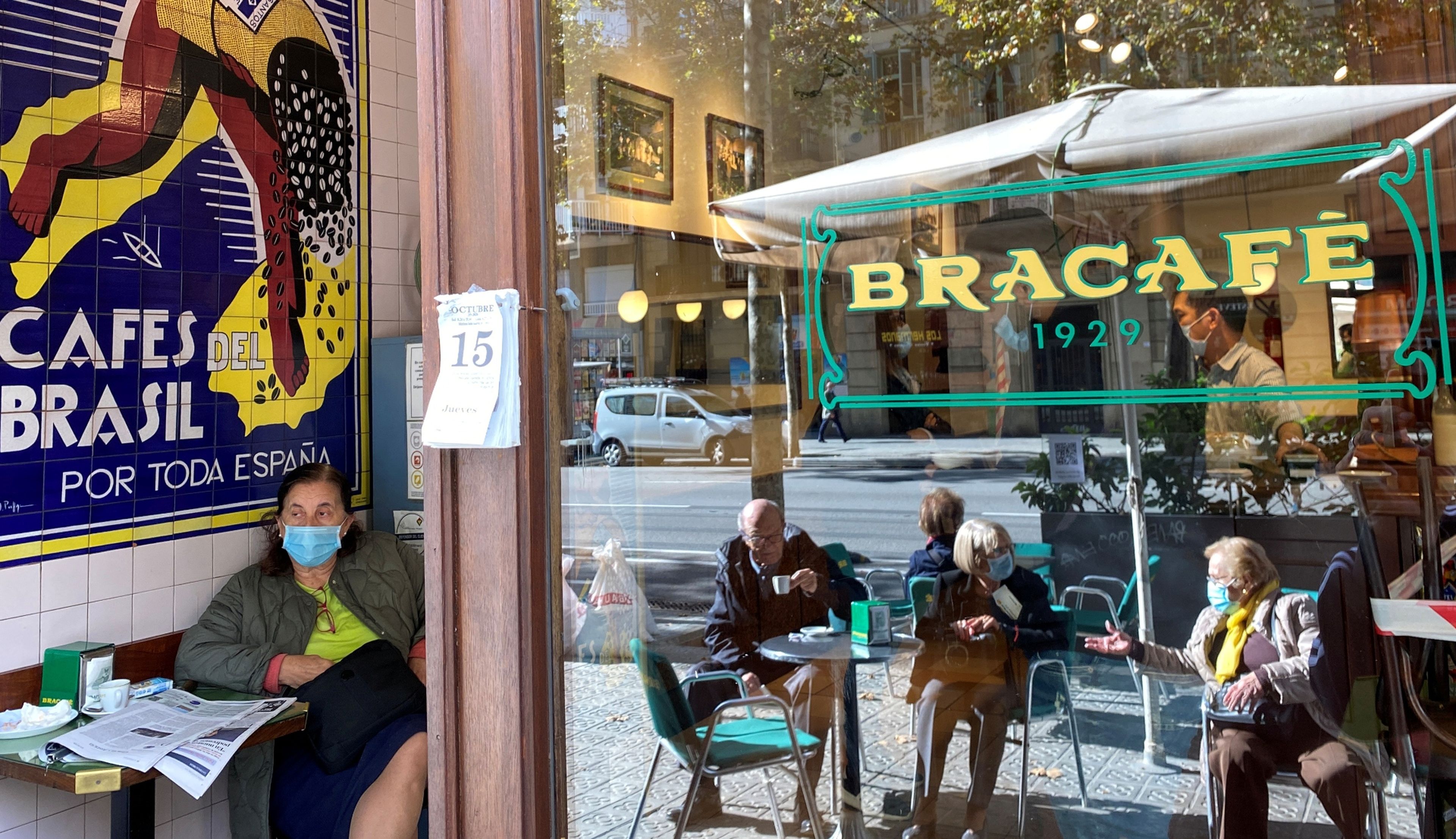 Varios clientes con mascarilla, en la terraza y el interior de un bar de Barcelona