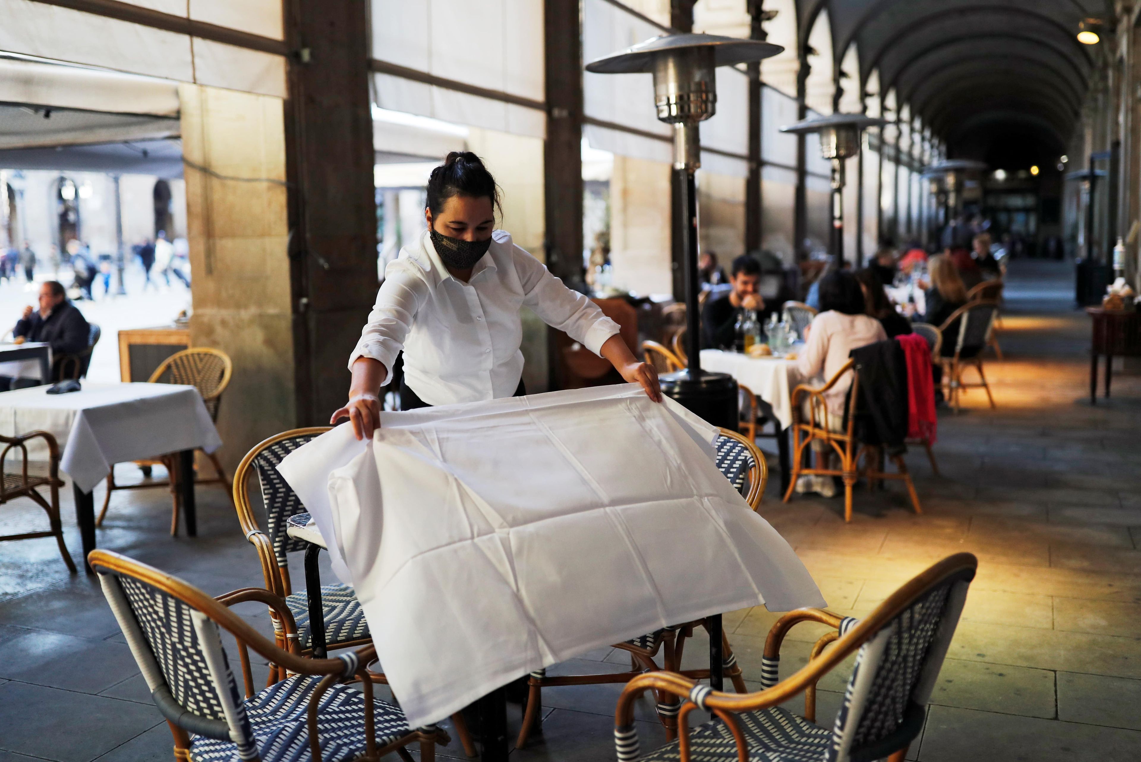 Camarera con mascarilla prepara una mesa en una terraza, en Barcelona.