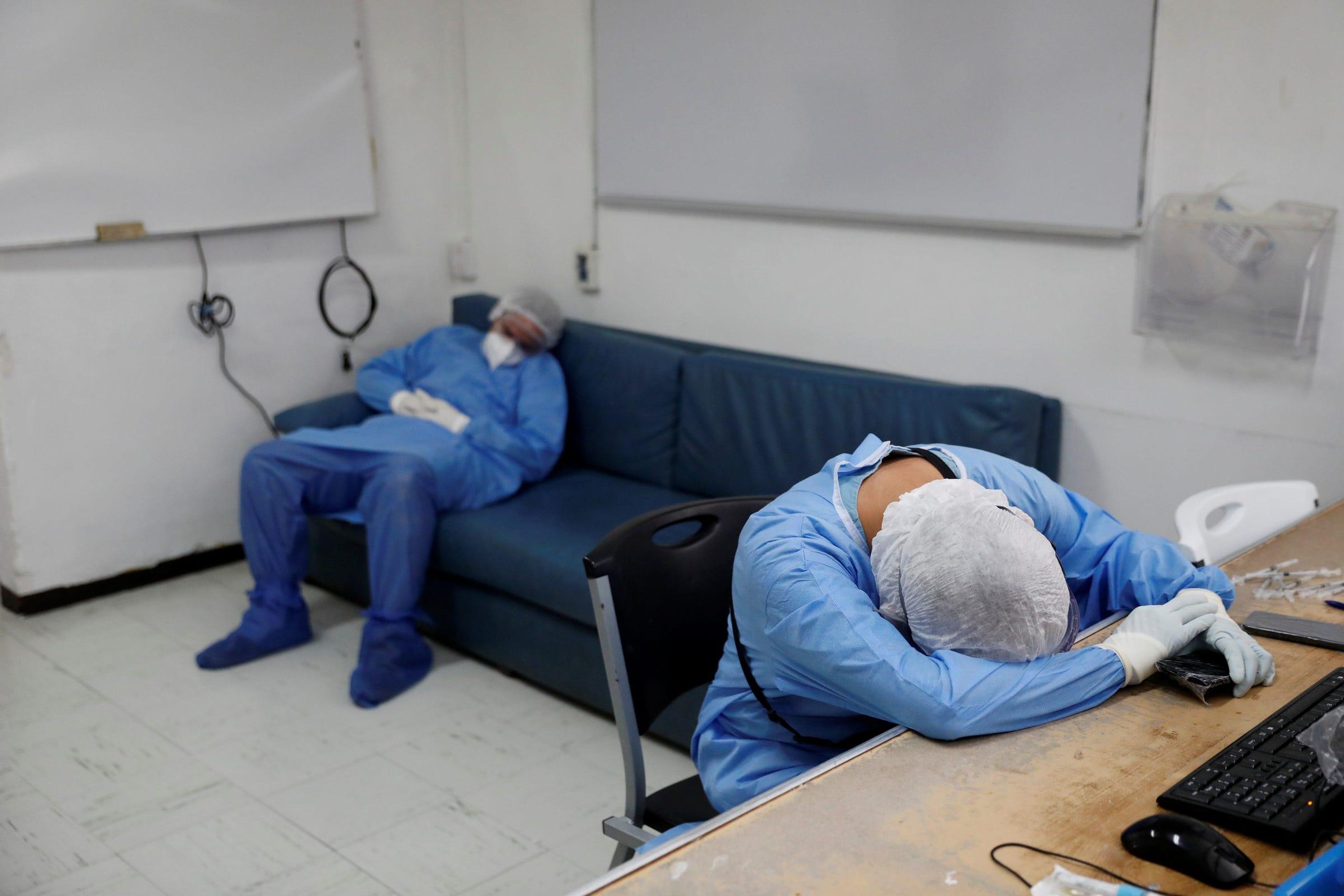 Los sanitarios con trajes protectores descansan después de horas de tratar a los pacientes.