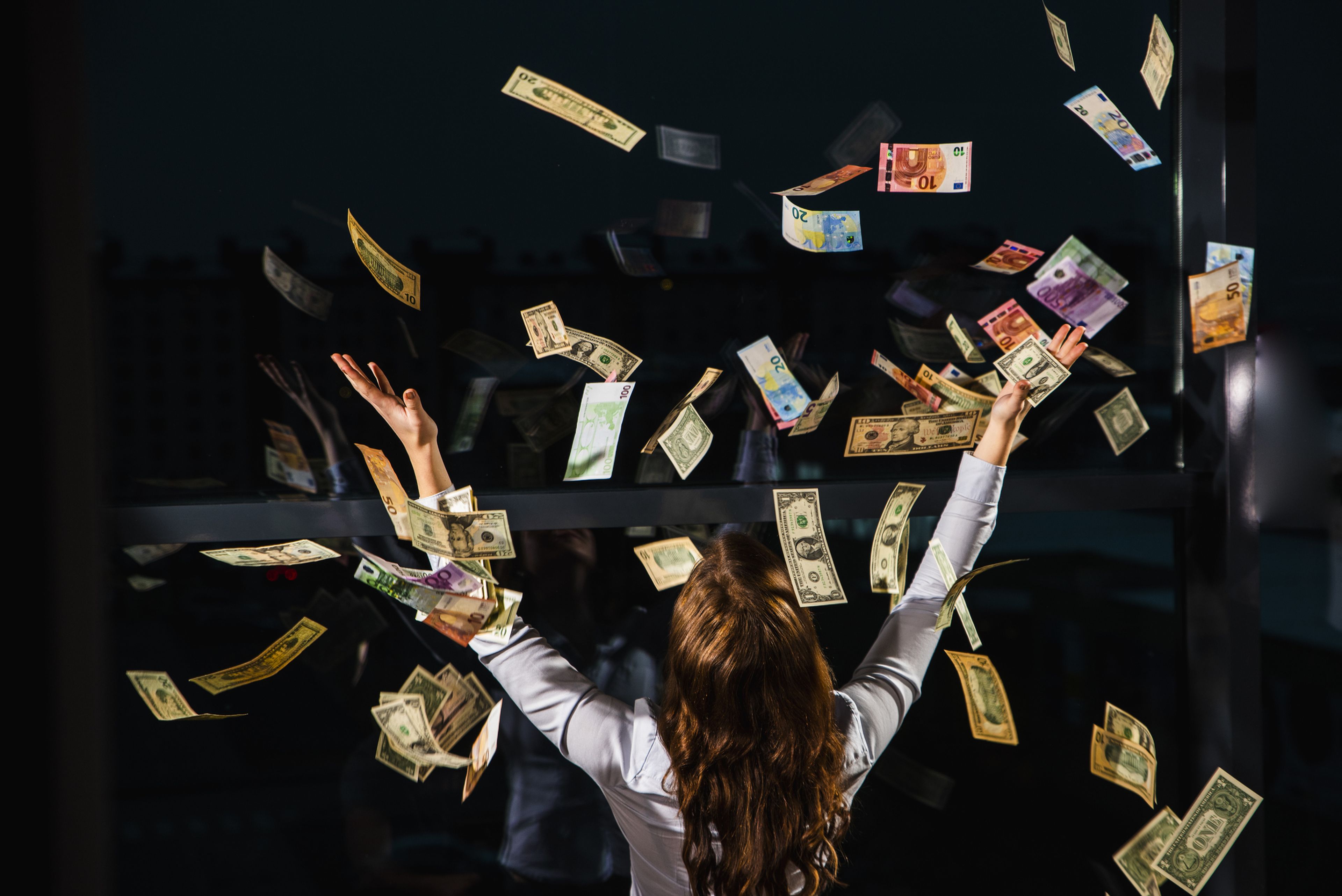 Una mujer con los brazos en alto, mientras billetes de dinero vuelan sobre ella.