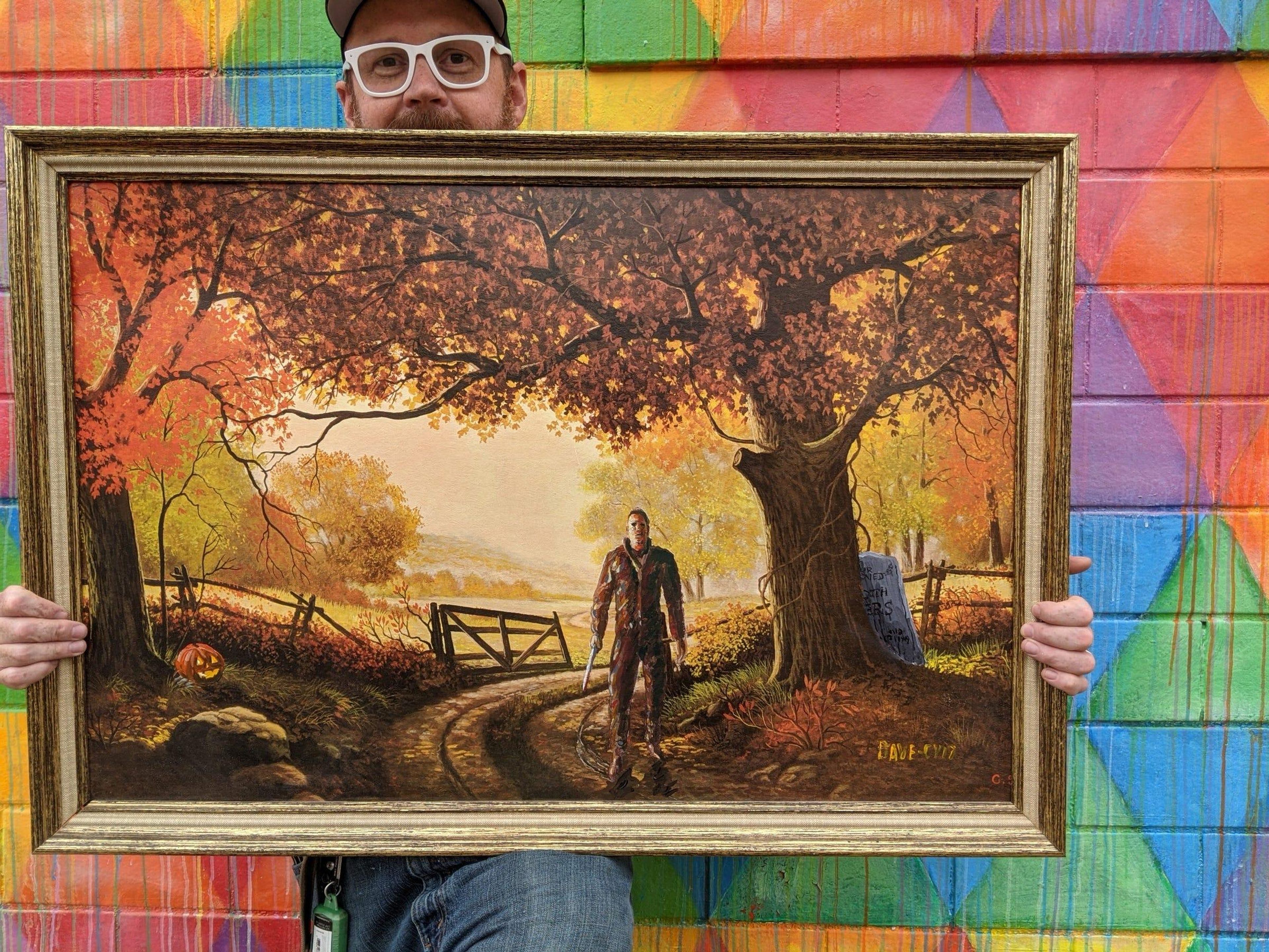 David Sherrill posa con un cuadro de Michael Myers, el antagonista de la saga 'Halloween', pintado sobre un sereno fondo otoñal.