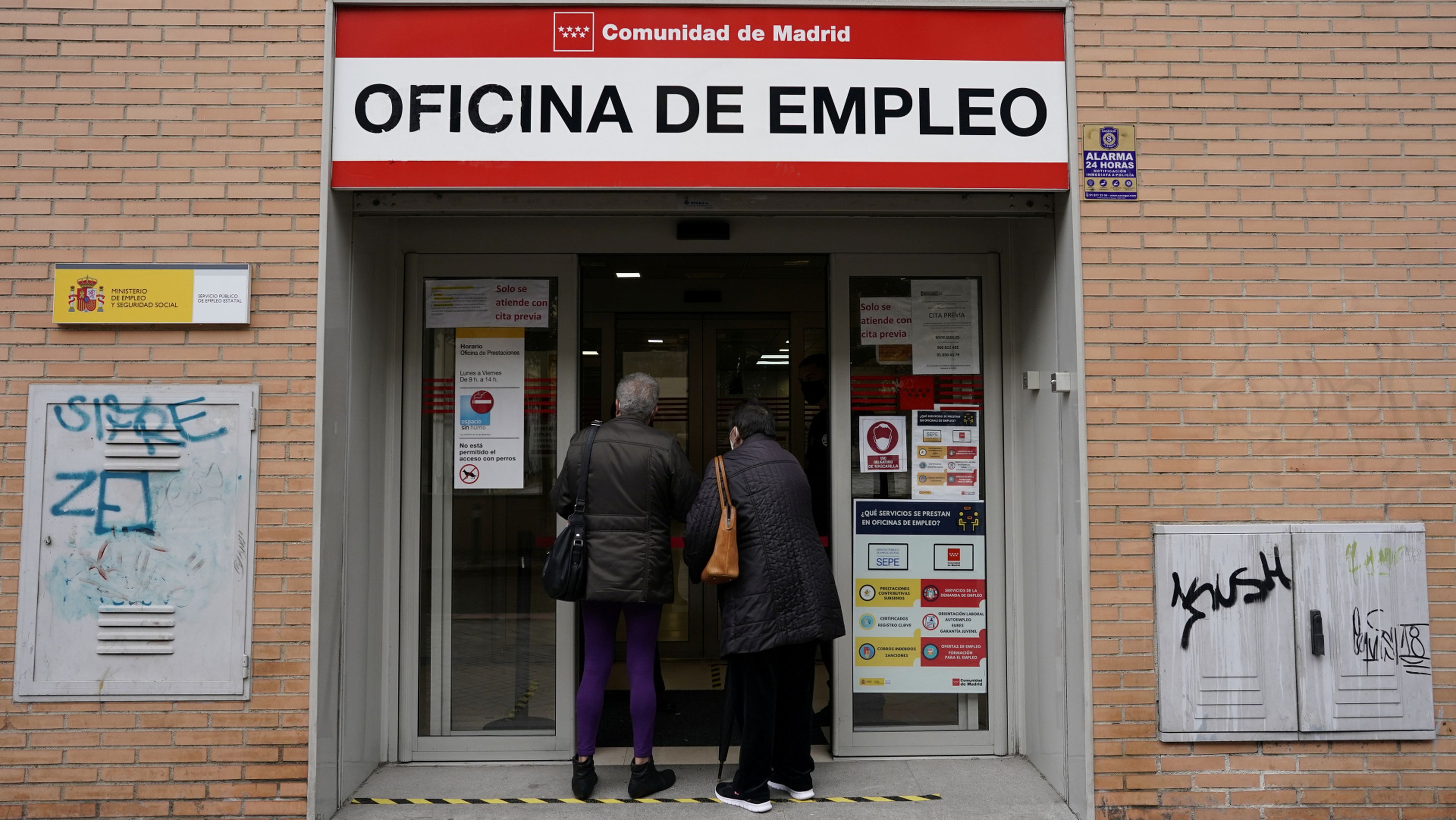 Dos desempleados con mascarilla hacen cola en una oficina de empleo en Madrid