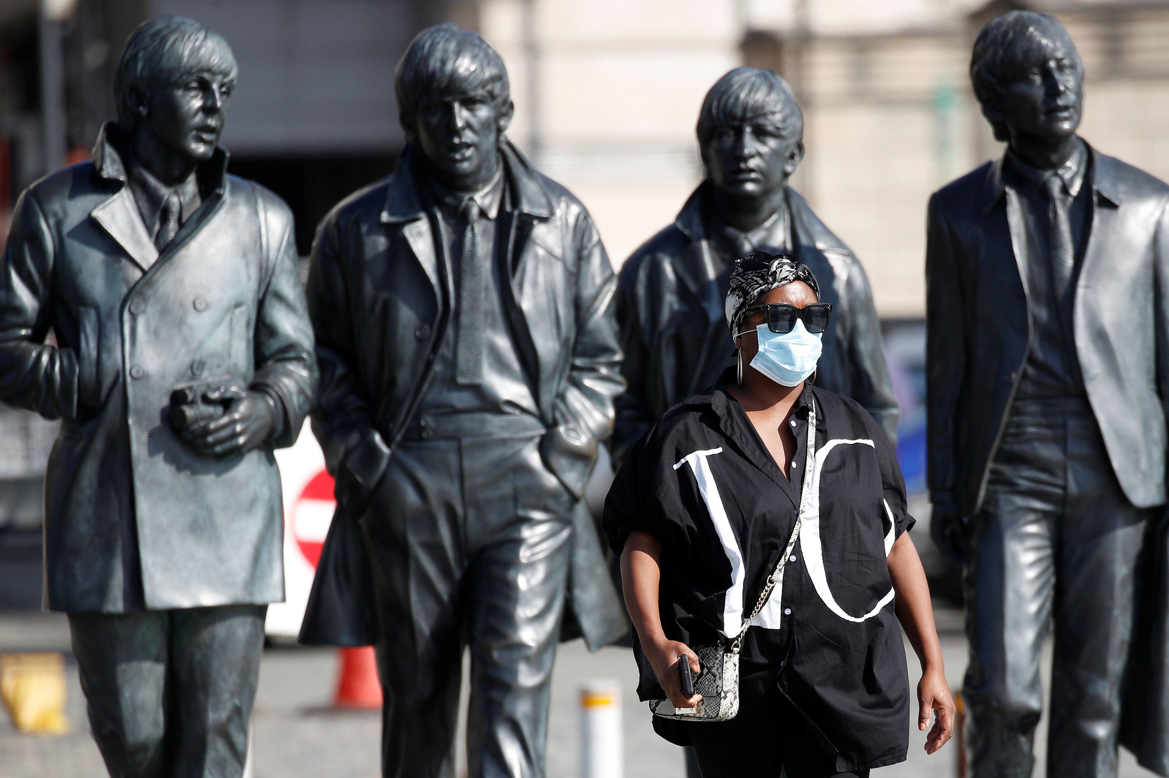 Una mujer camina delante de una estatua de los Beatles en Liverpool.