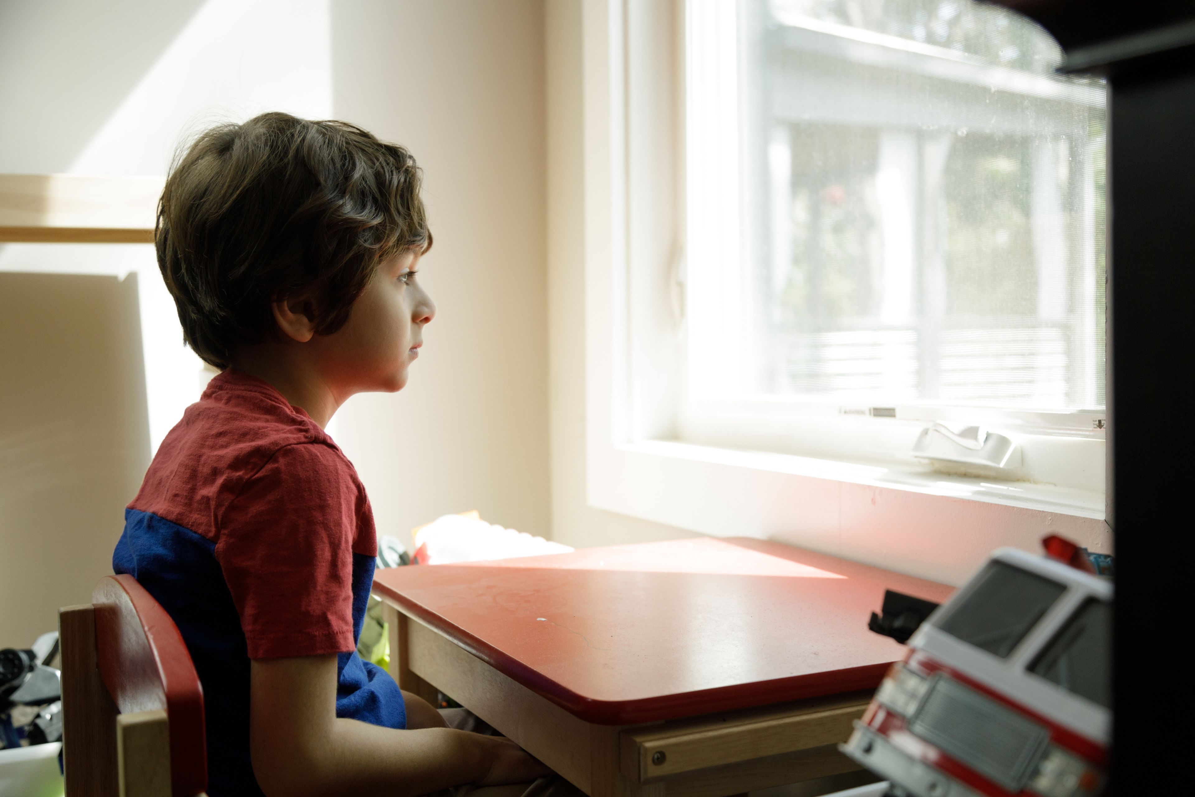 Un niño mira por la ventana sentado en una mesa de estudio.