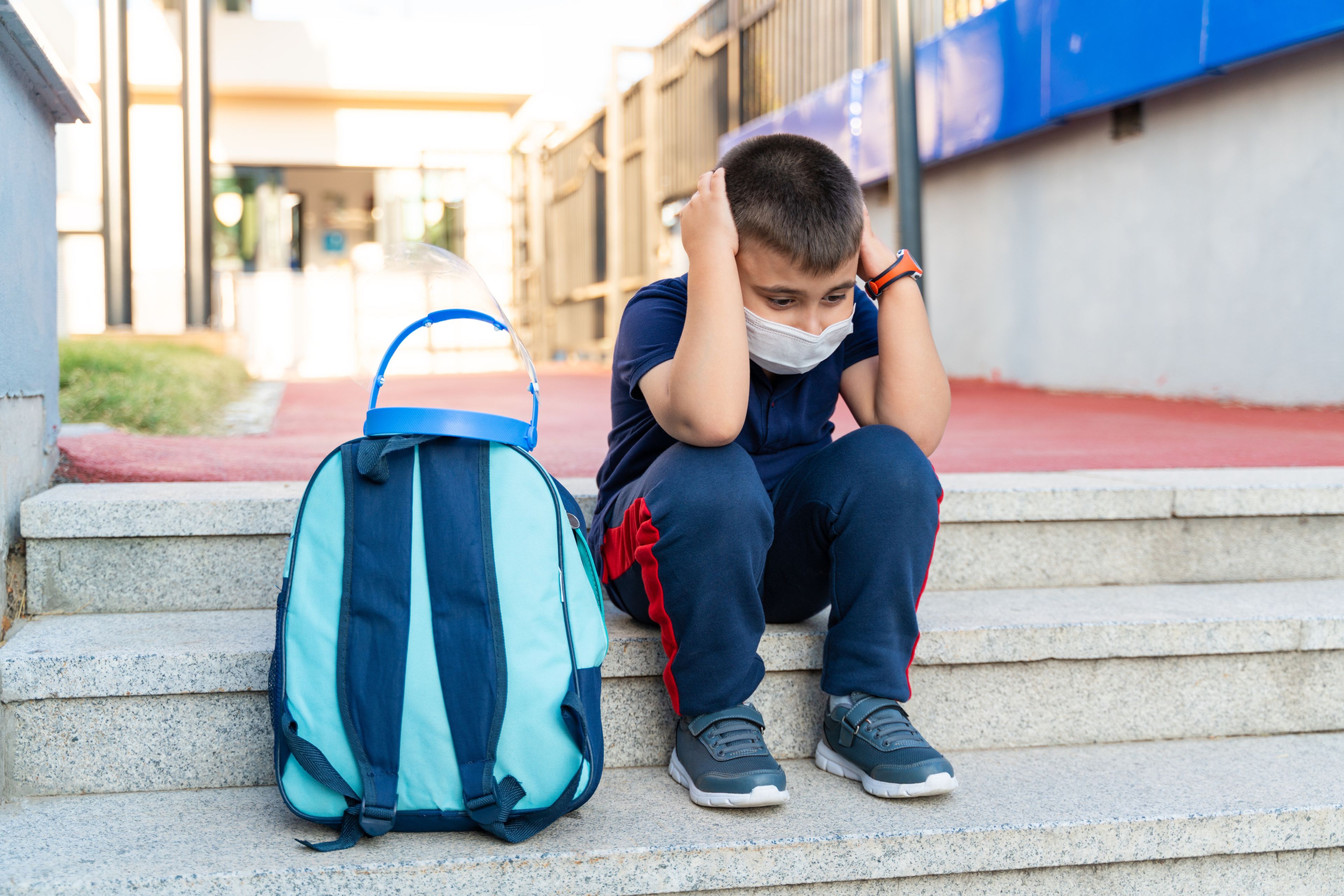 Un niño se muestra triste con la mochila al lado.
