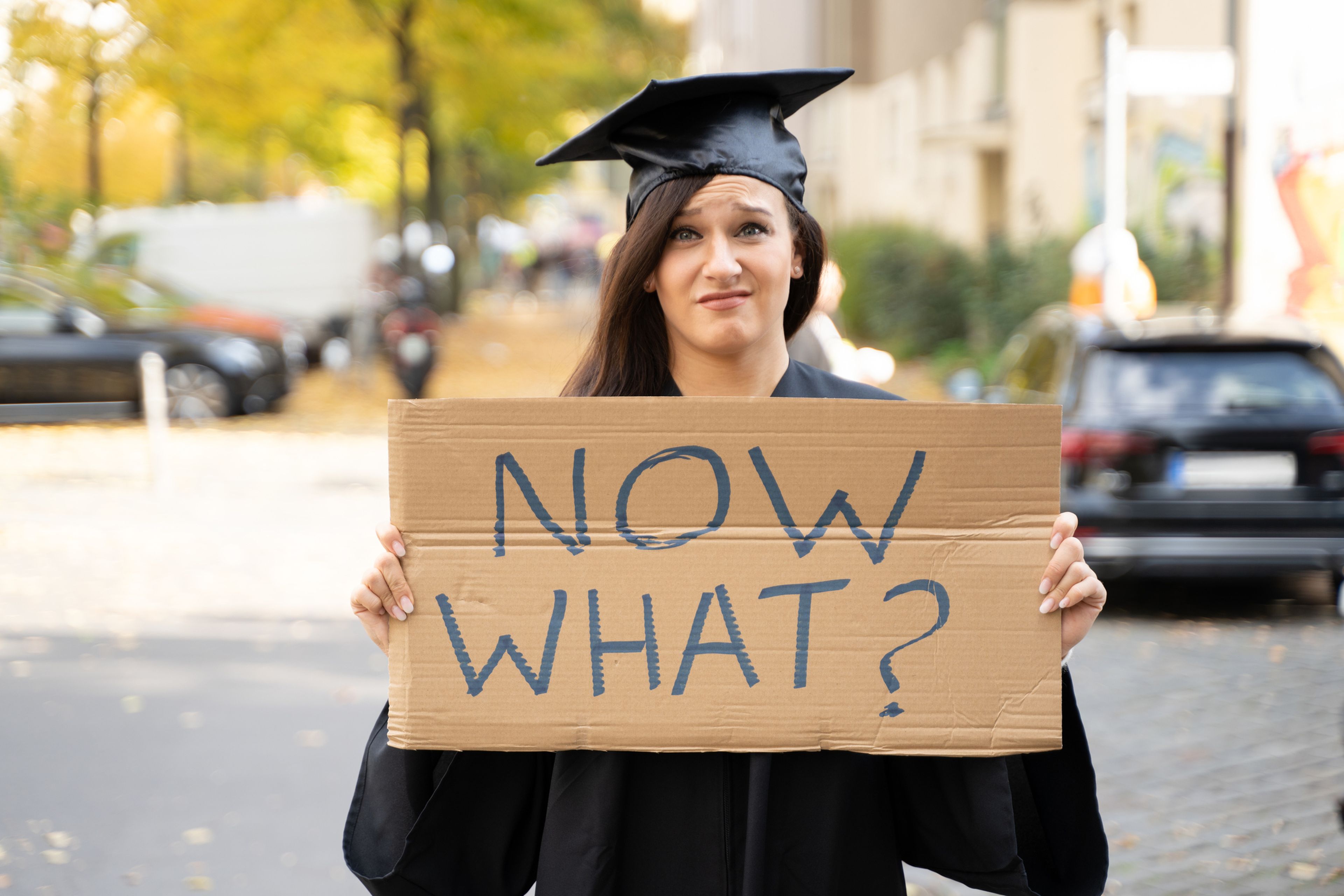 Una recién graduada enseña un cartel en el que se lee "¿y ahora qué?".