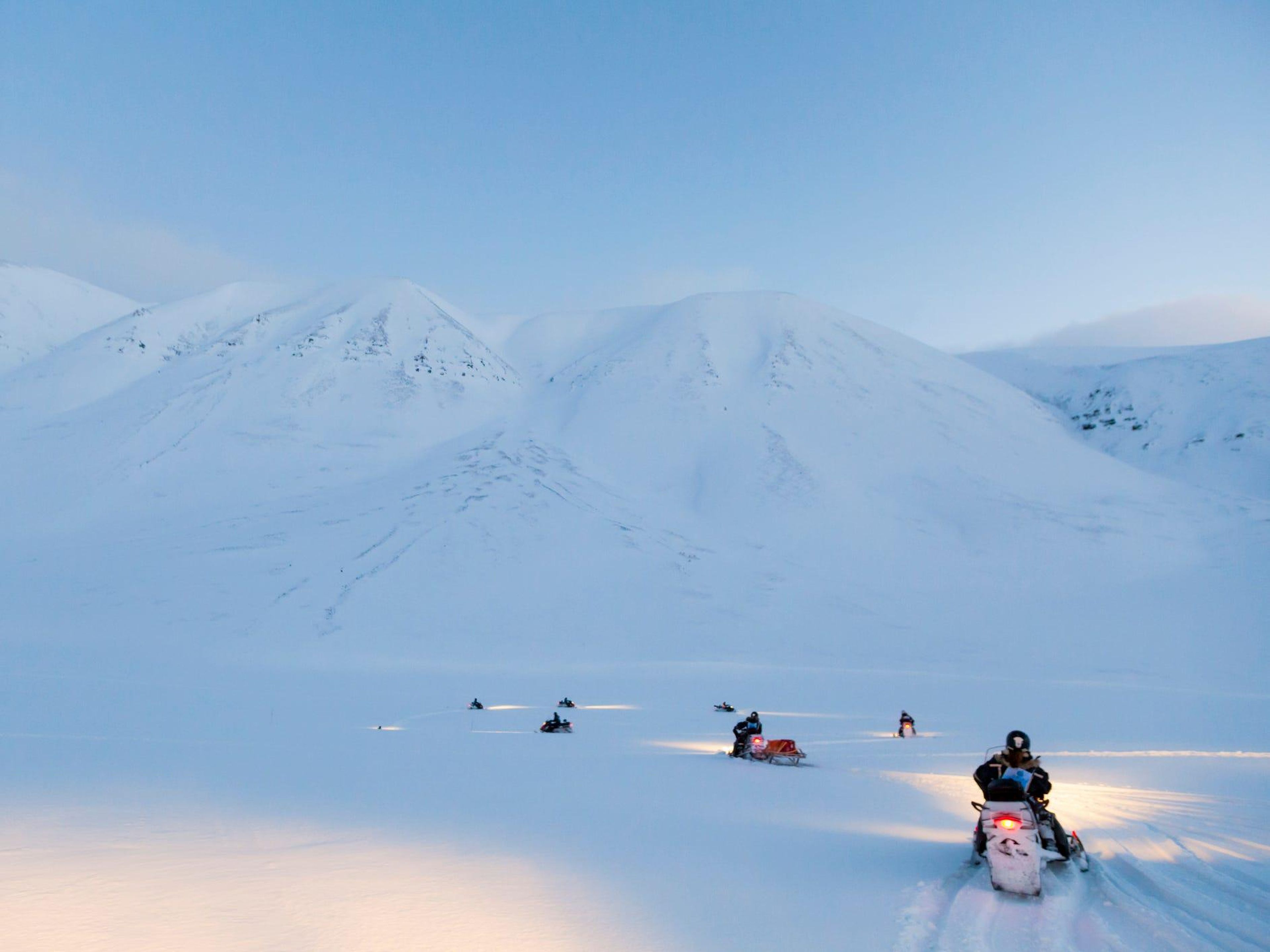 Estudiantes conduciendo sus motos de nieve durante un curso de formación en Adventdalen, Svalbard.