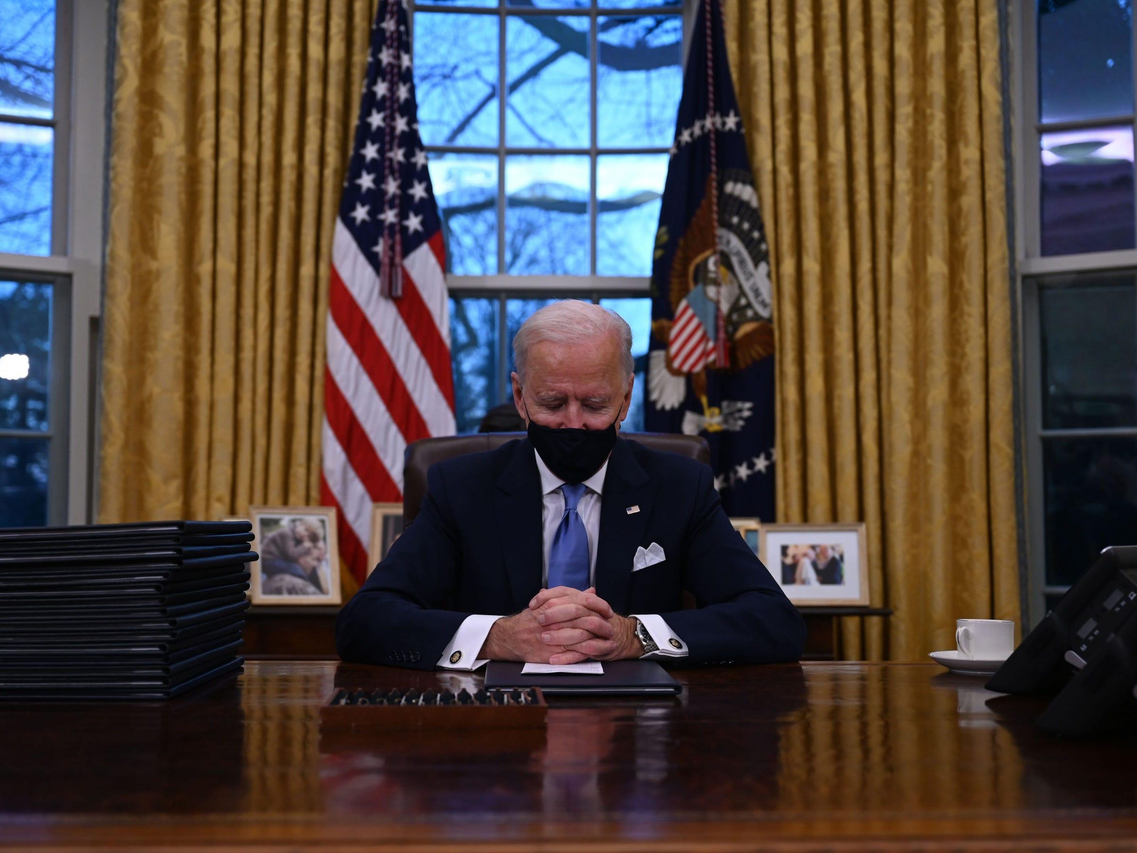 El presidente Biden se sienta frente a una bandera estadounidense y otra de sello presidencial.