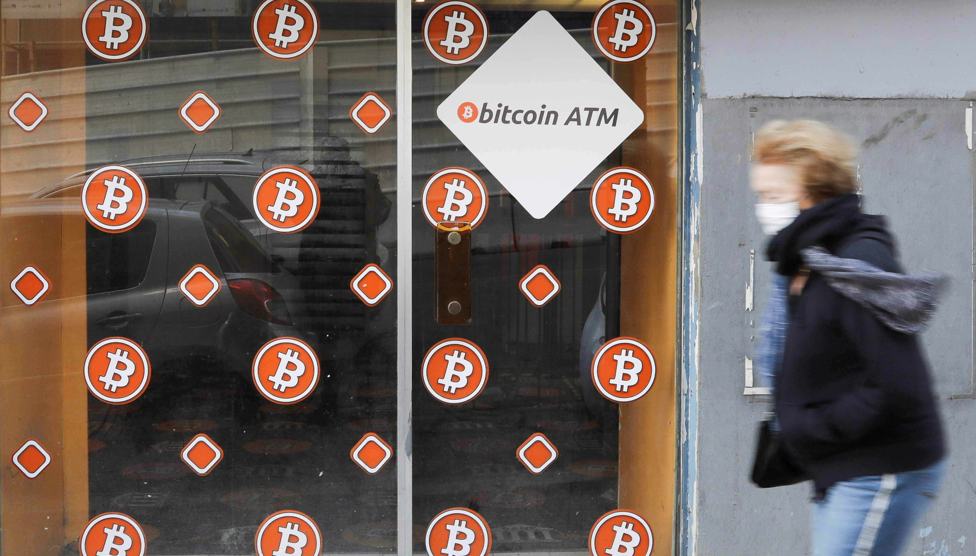 Una mujer con mascarilla pasa ante un cajero autómatíco de bitcoin en Marsella (Francia)
