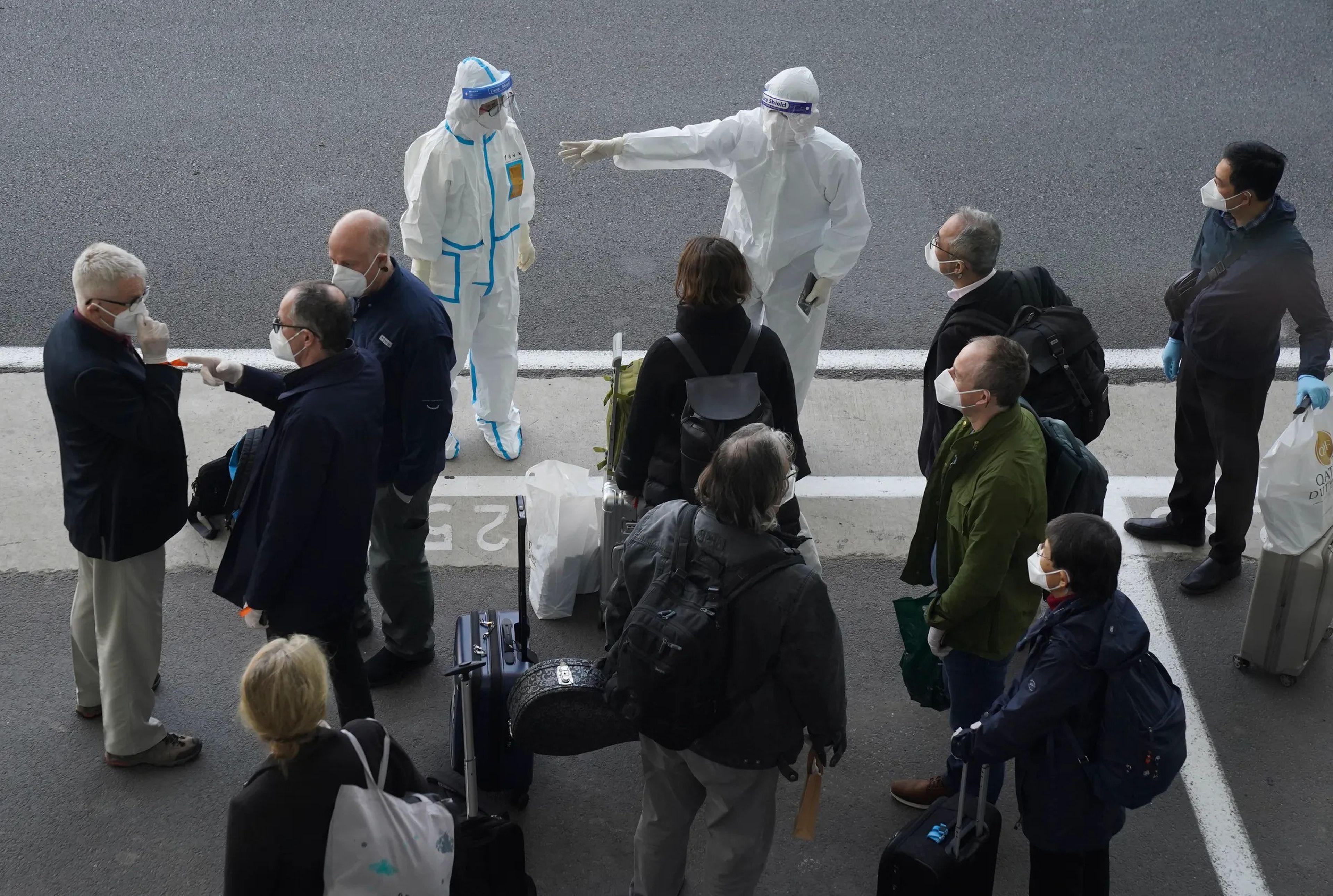 A worker in protective GEAR directs members of the World Health Organization team at the airport in Wuhan, China, January 14, 2021.