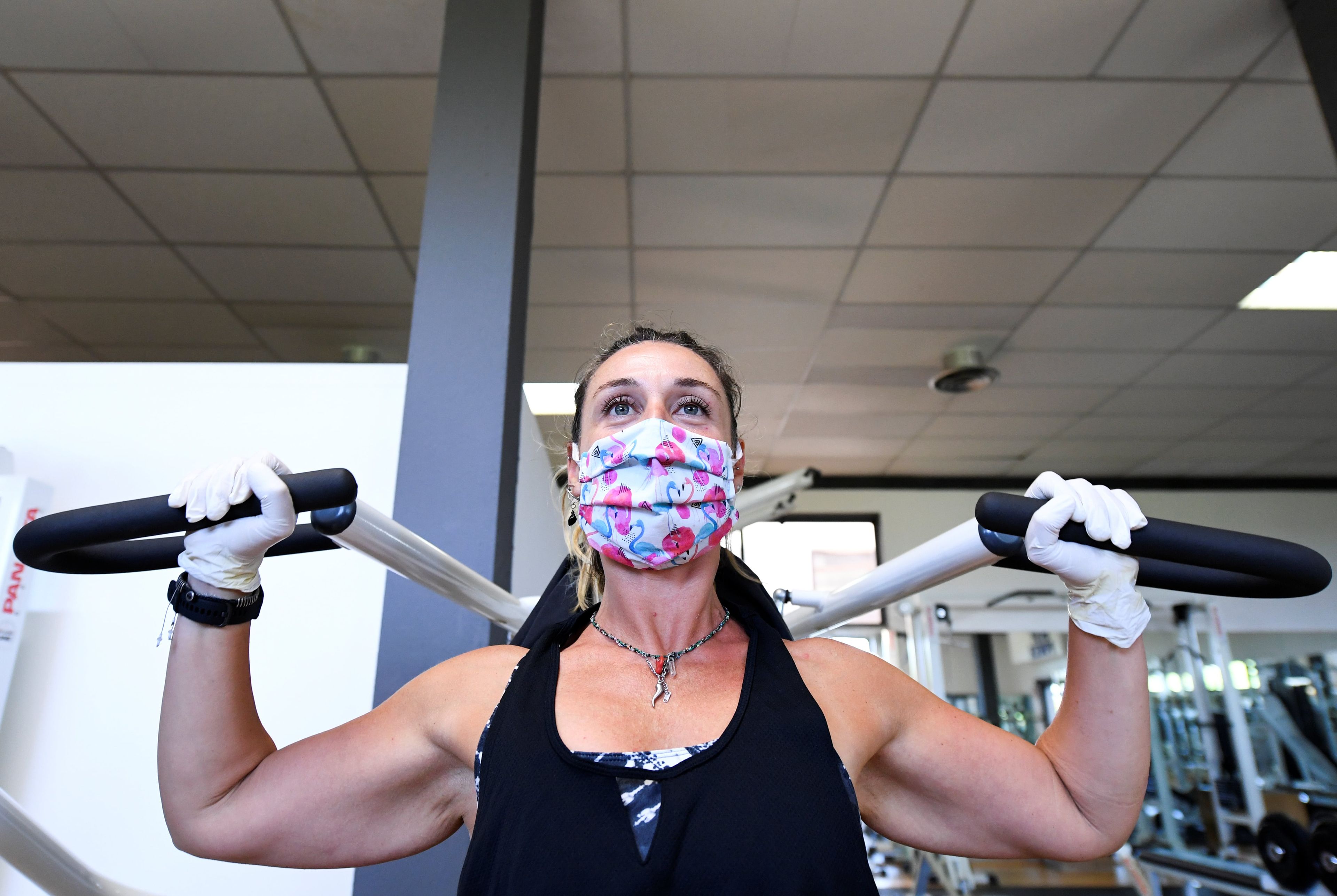 Mujer haciendo pesas con mascarilla y guantes en un gimnasio.