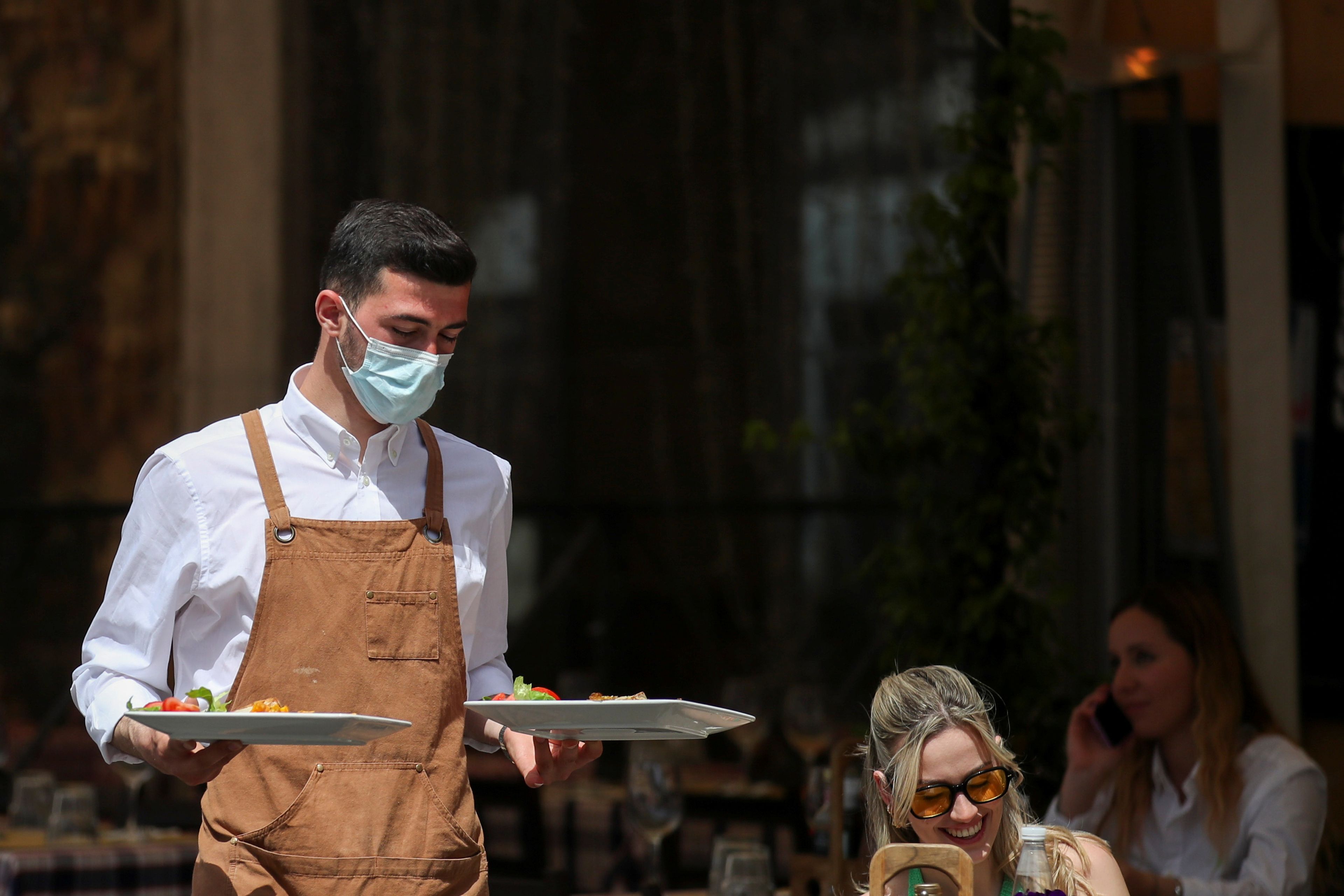 Camarero con mascarilla sirve en una terraza en Roma, Italia.