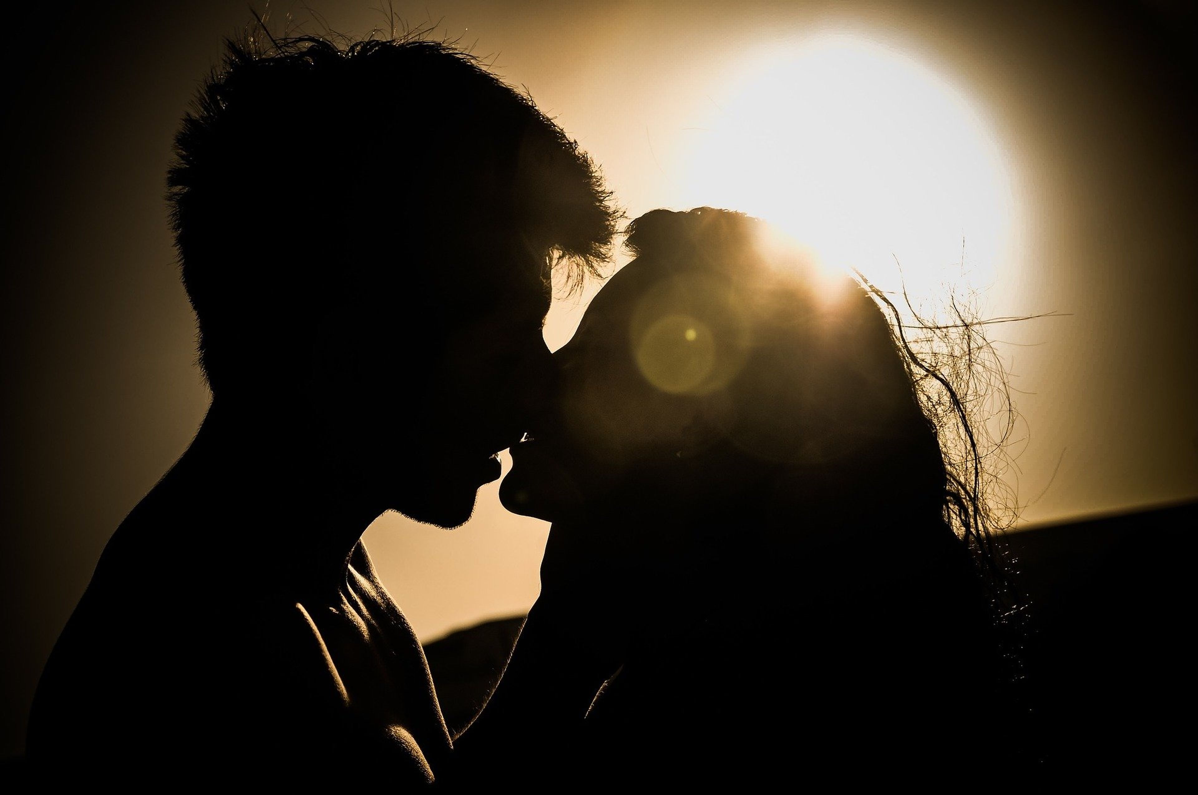Un chico y una chica se besan ante una puesta de sol.