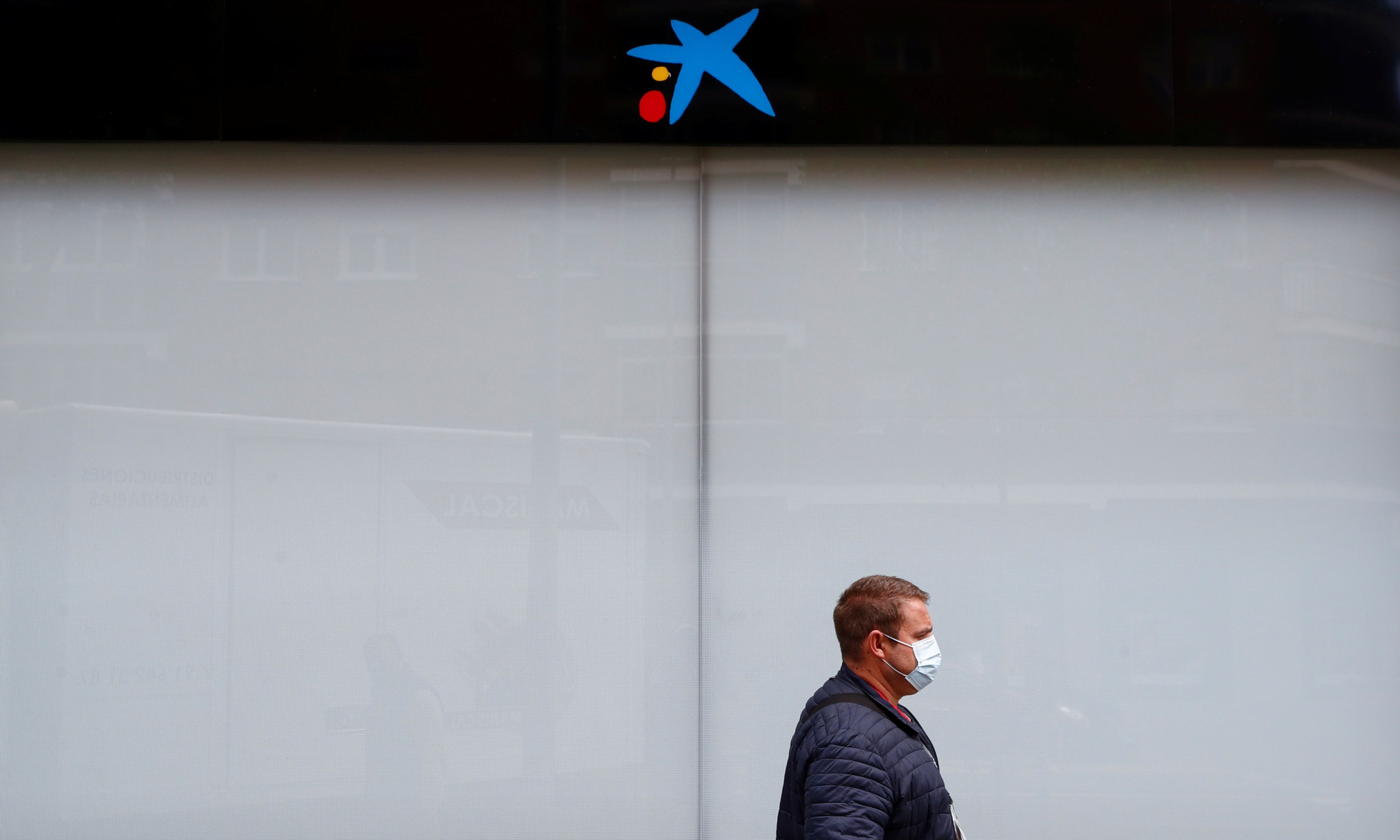 Un hombre con mascarilla pasa ante una oficina cerrada de CaixaBank