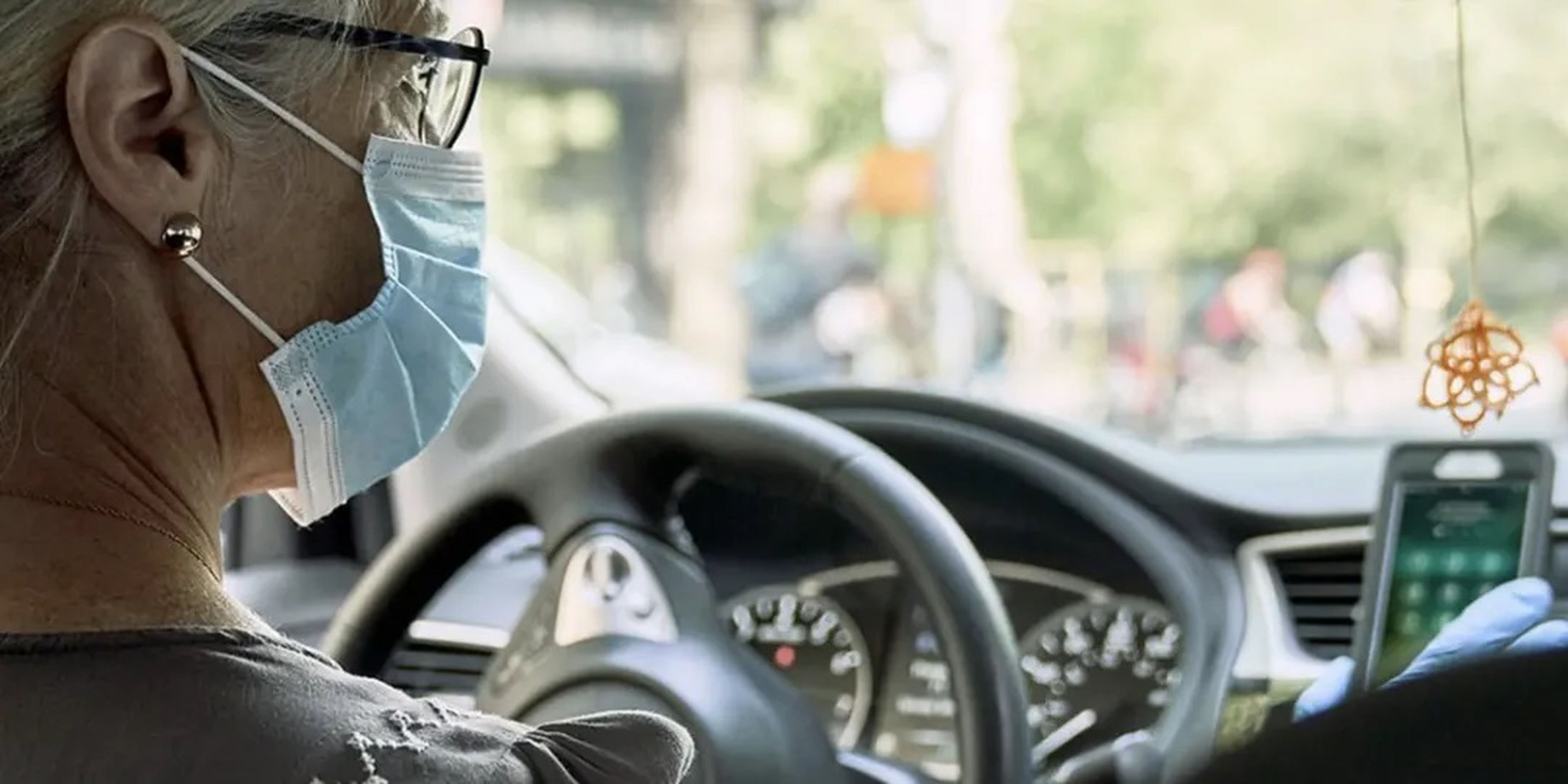 Una mujer con mascarilla y guantes conduce un coche.