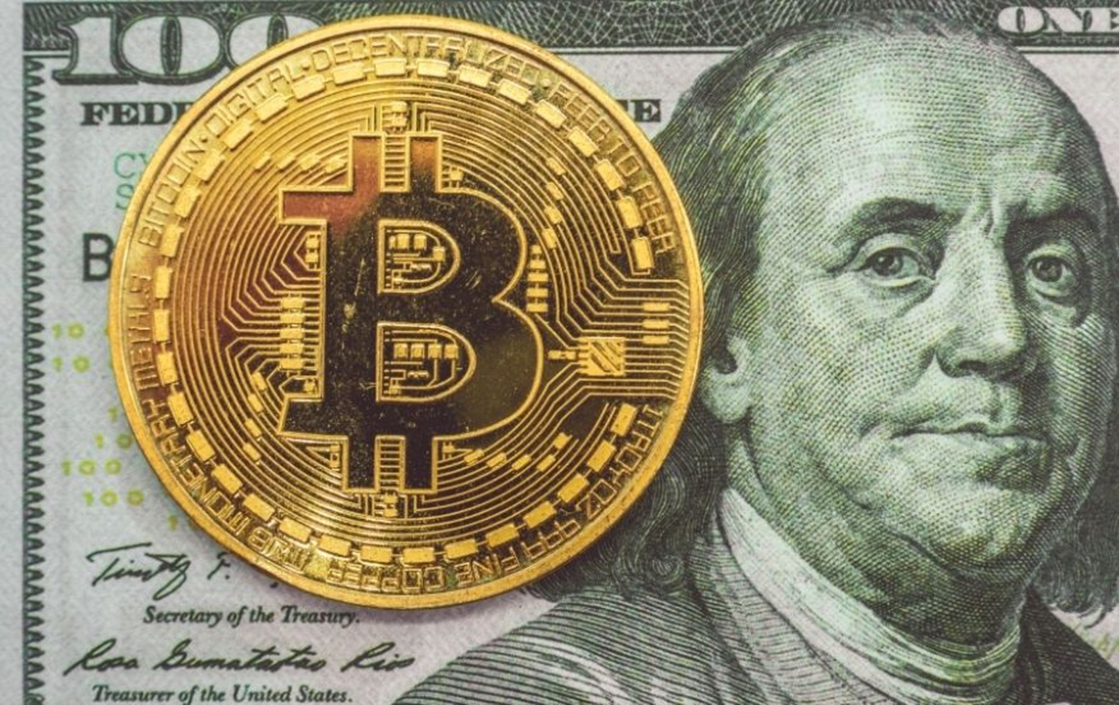 Un bitcoin sobre un billete de 100 dólares.