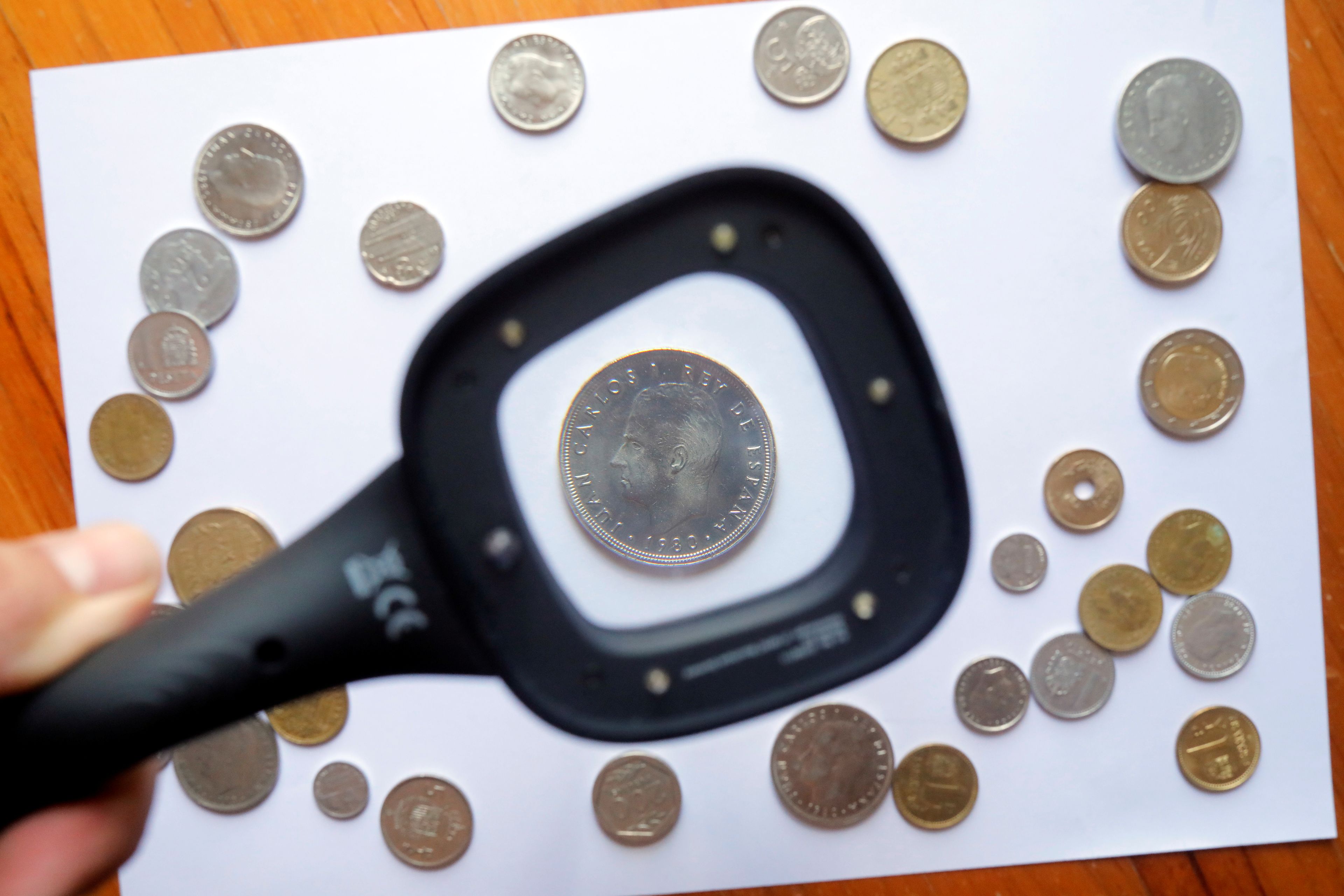 Un hombre mira una moneda de peseta con una lupa