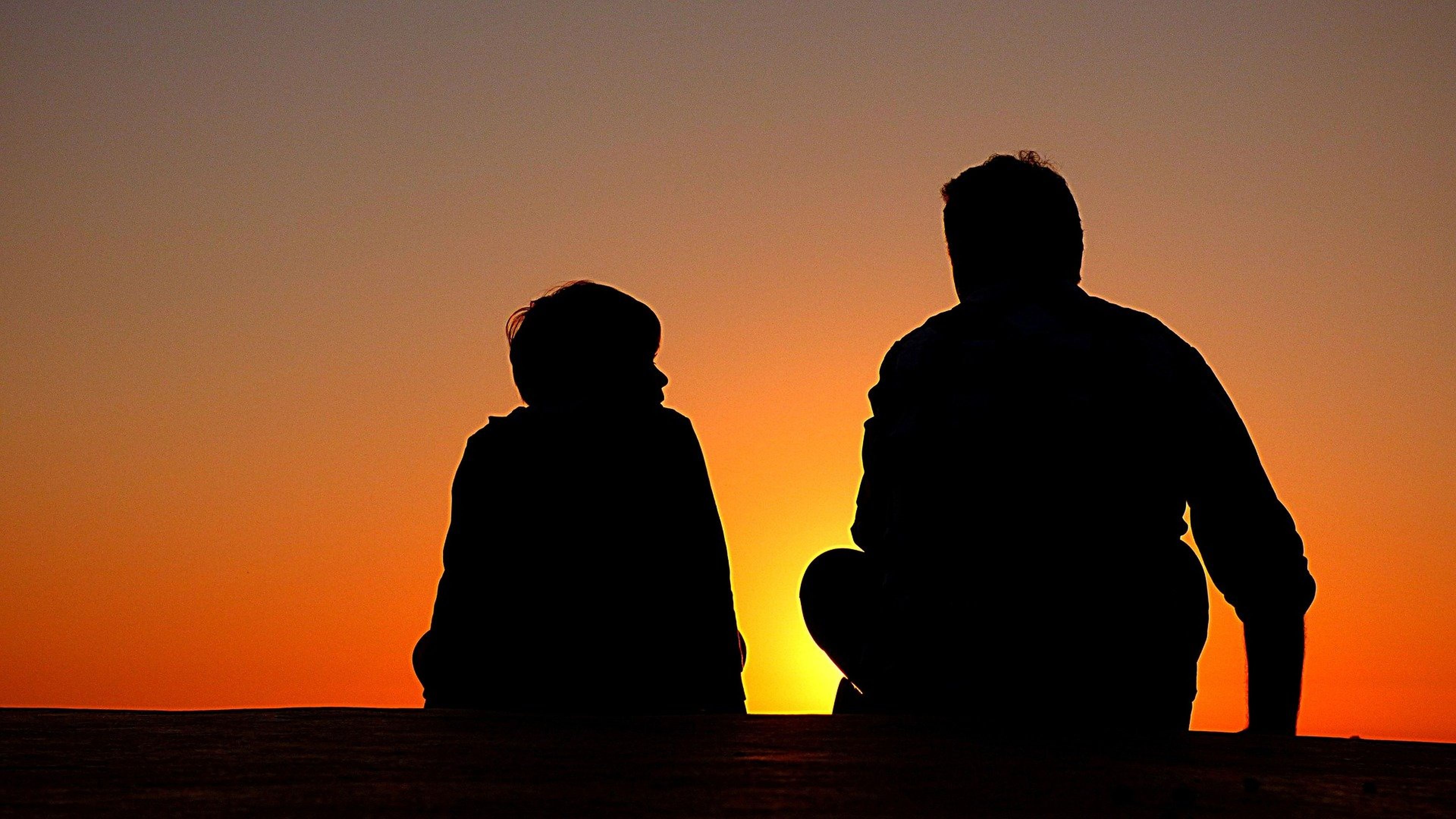 Un hombre y un niño ante una puesta de sol.