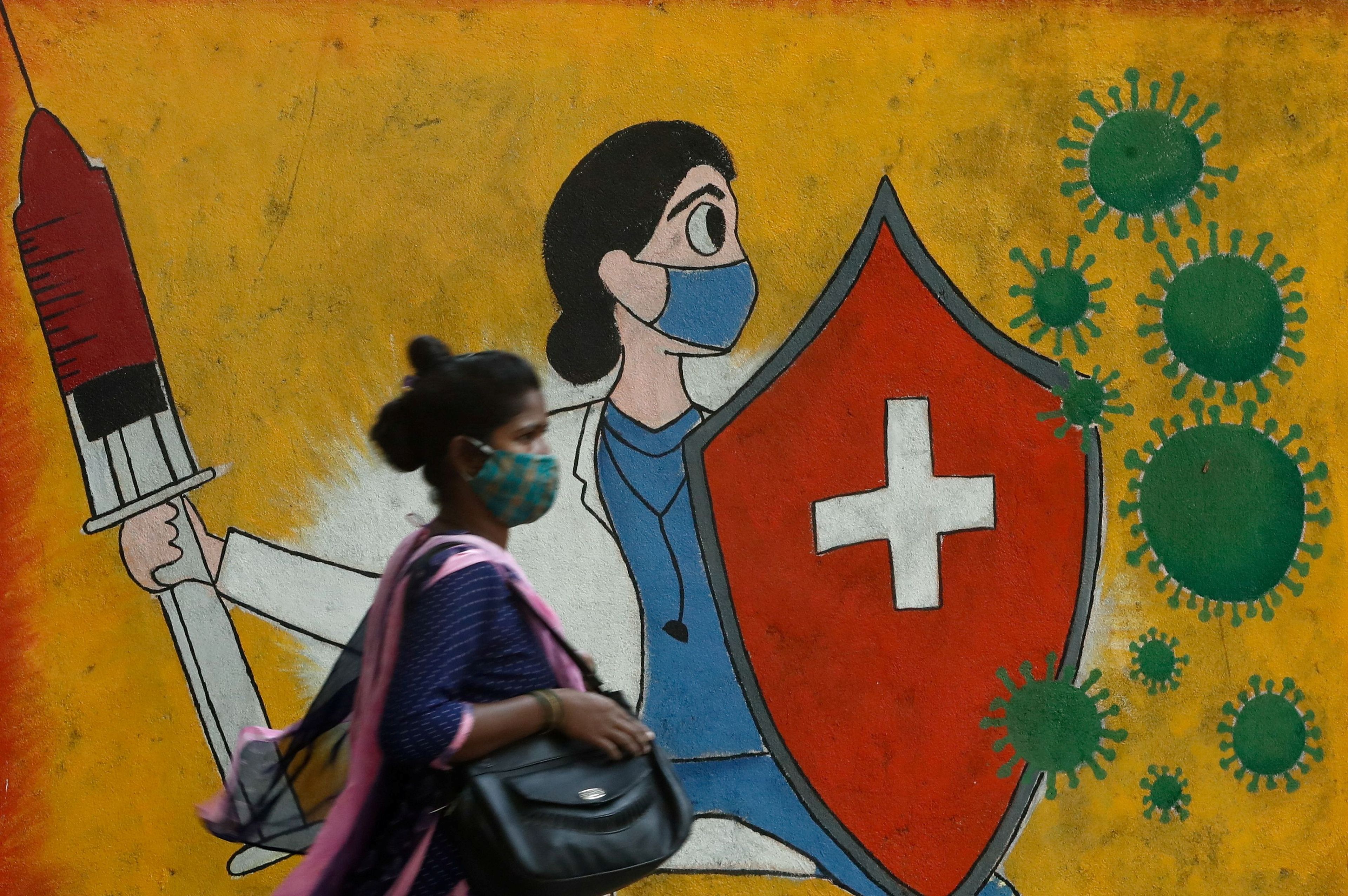 Una mujer camina delante de un mural sobre el coronavirus en Mumbai