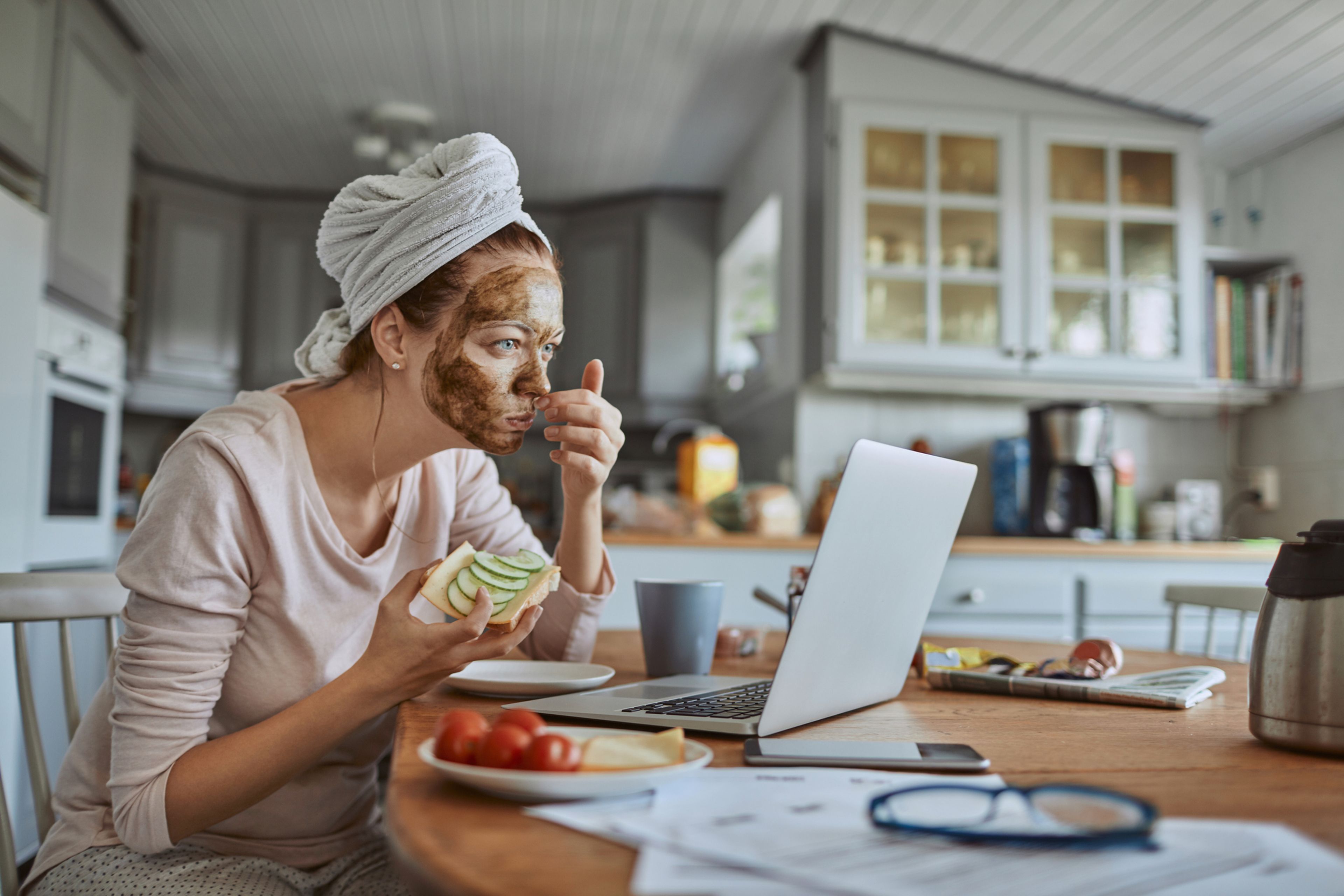 Una mujer come sano delante del ordenador con una mascarilla puesta.