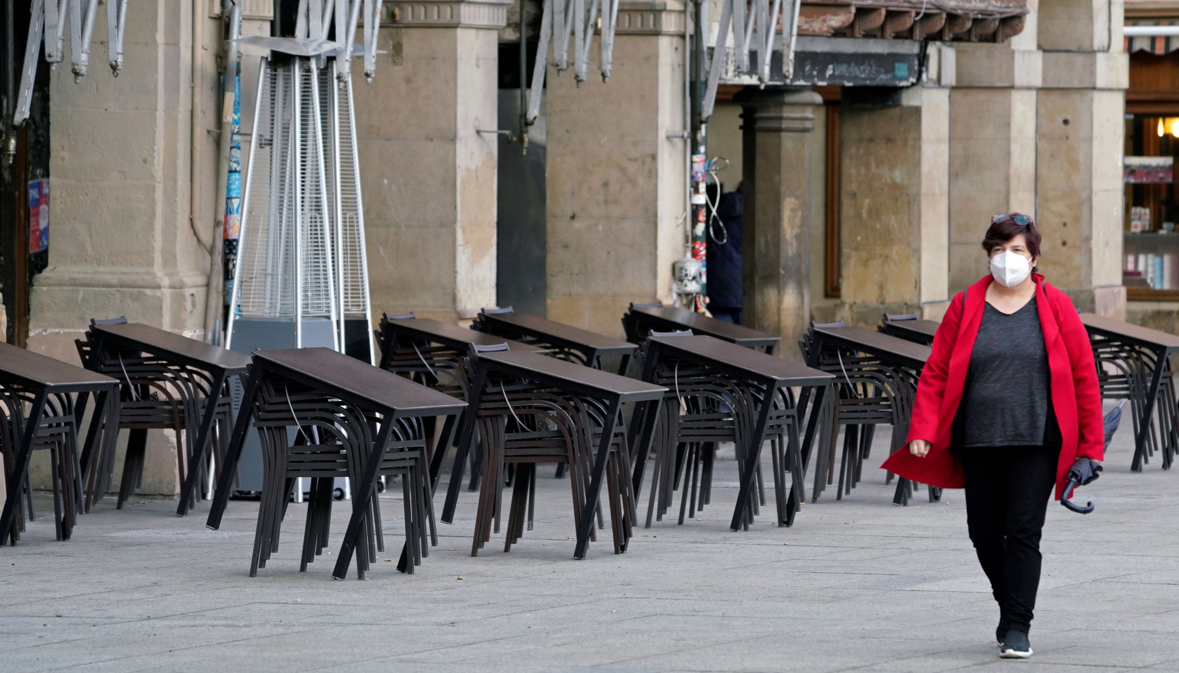 Una mujer con mascarilla pasa ante la terraza de un bar cerrado en Pamplona