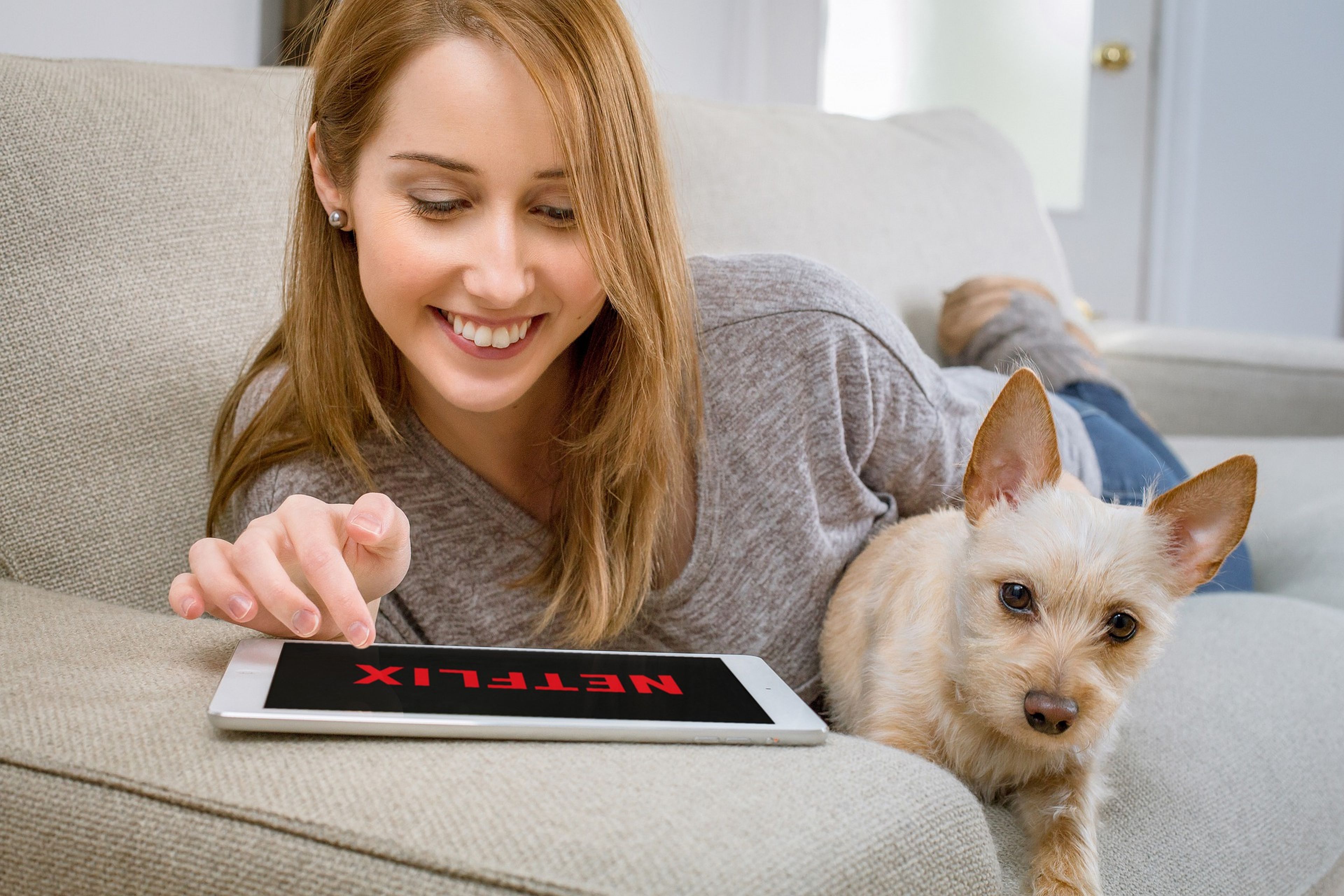 Una mujer con su perro abre Netflix en una tablet.