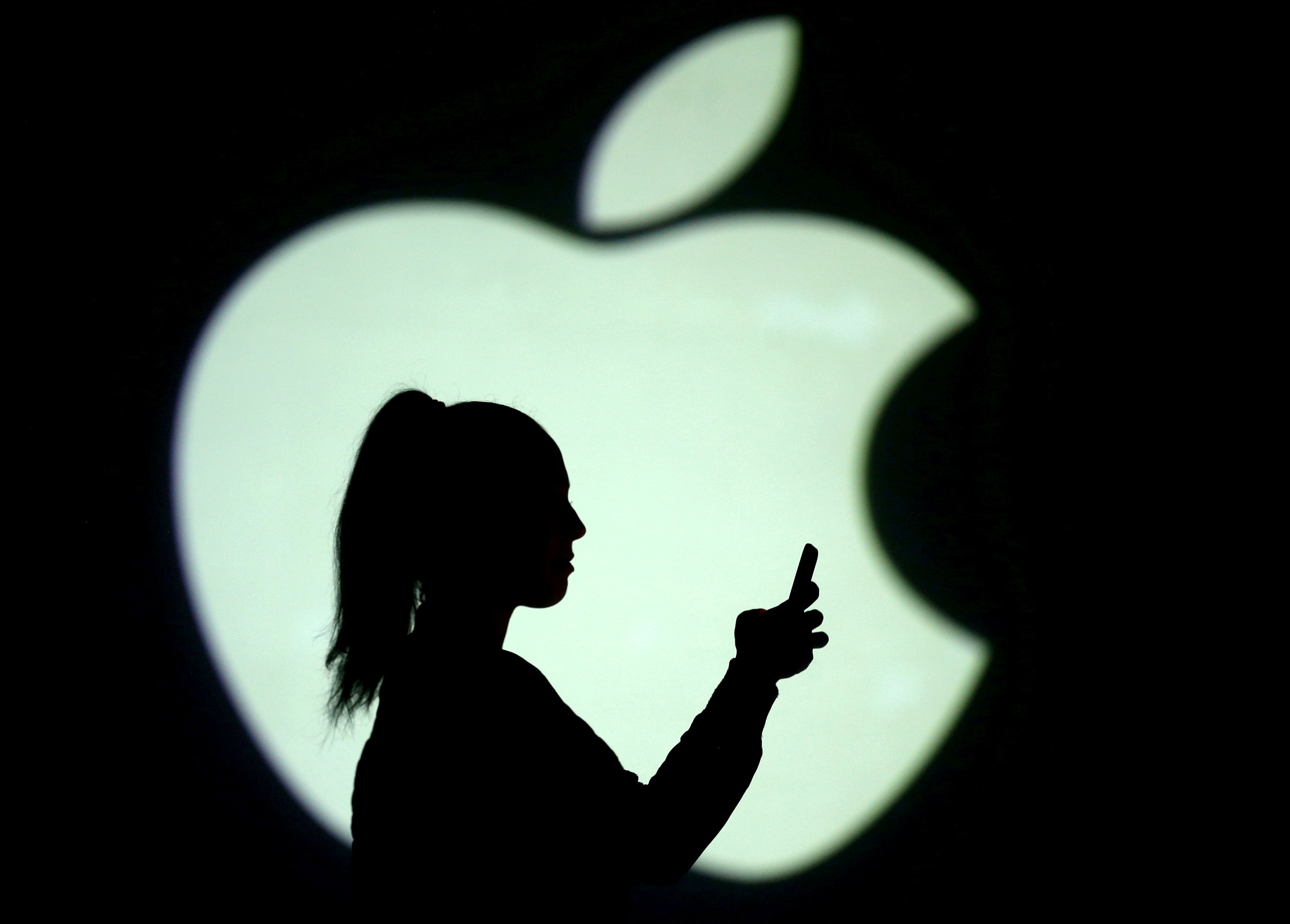Una mujer utiliza un teléfono móvil delante de un logotipo de Apple