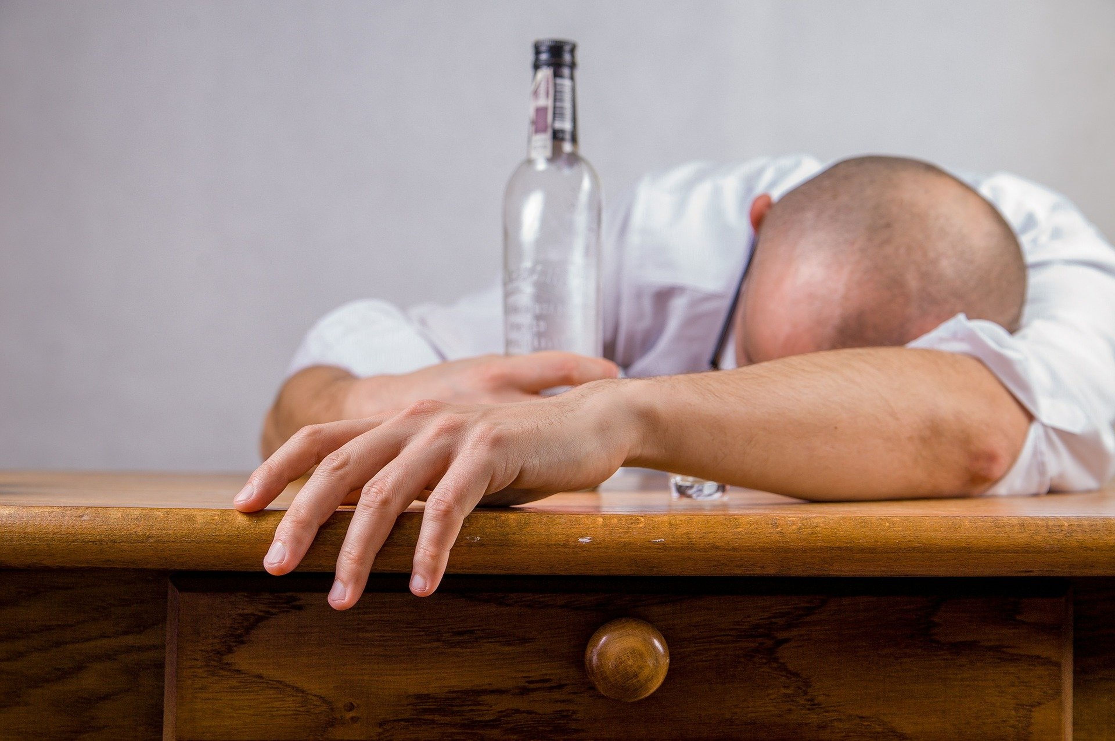 Una persona tirada en una mesa con una botella de alcohol.