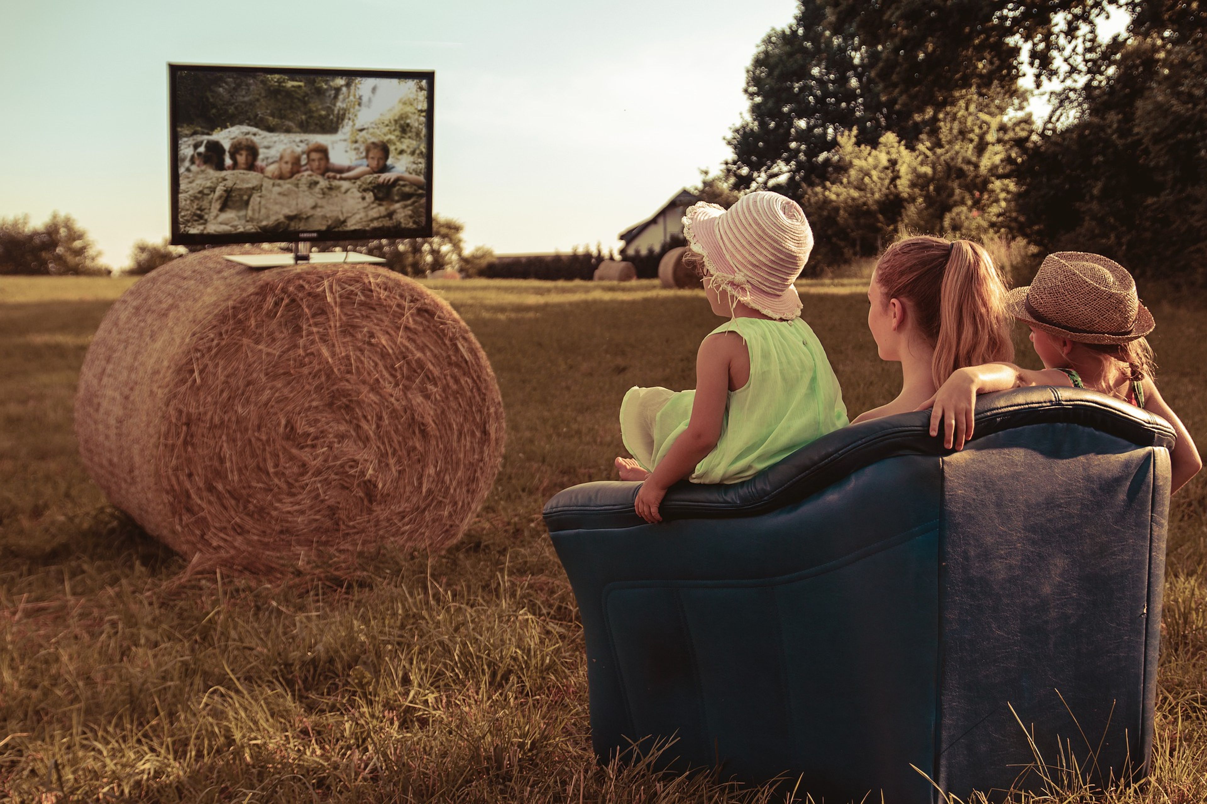 Tres niñas ven la televisión en el campo.