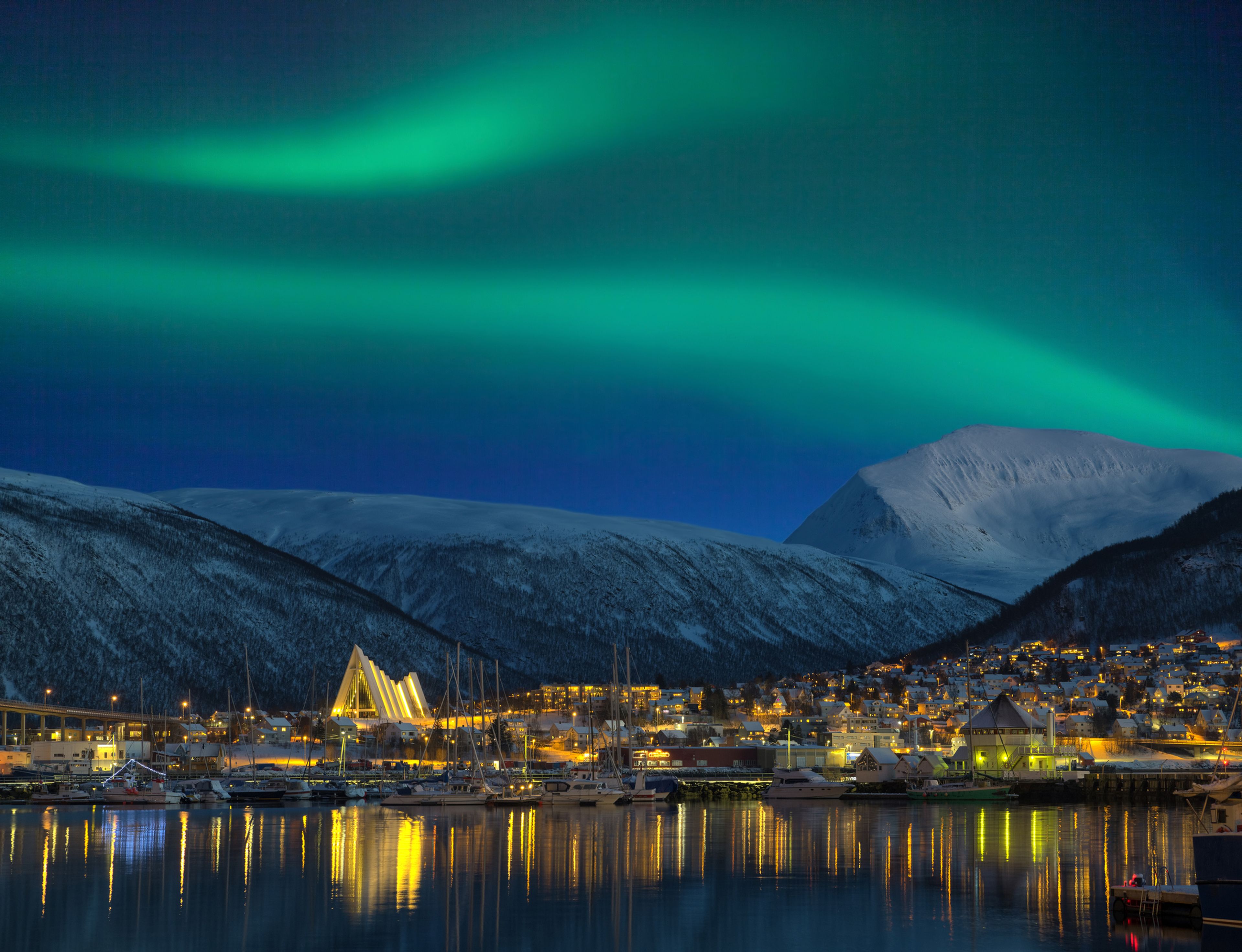 La ciudad de Tromso por la noche iluminada por una aurora boreal.